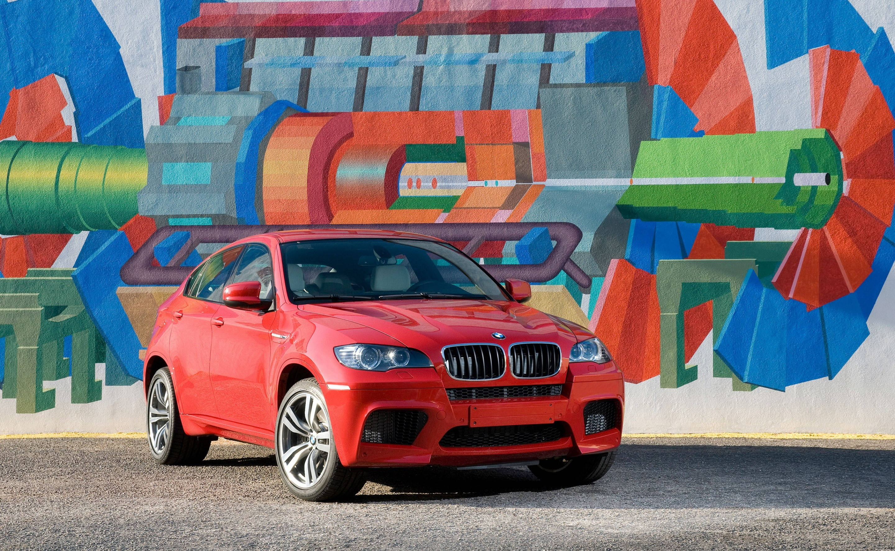 BMW X6 M塗鴉牆背景 壁紙 — 一輛鮮紅色的BMW X6 M大膽地矗立在色彩繽紛的抽象壁畫前，壁畫帶有幾何形狀和大膽色調。