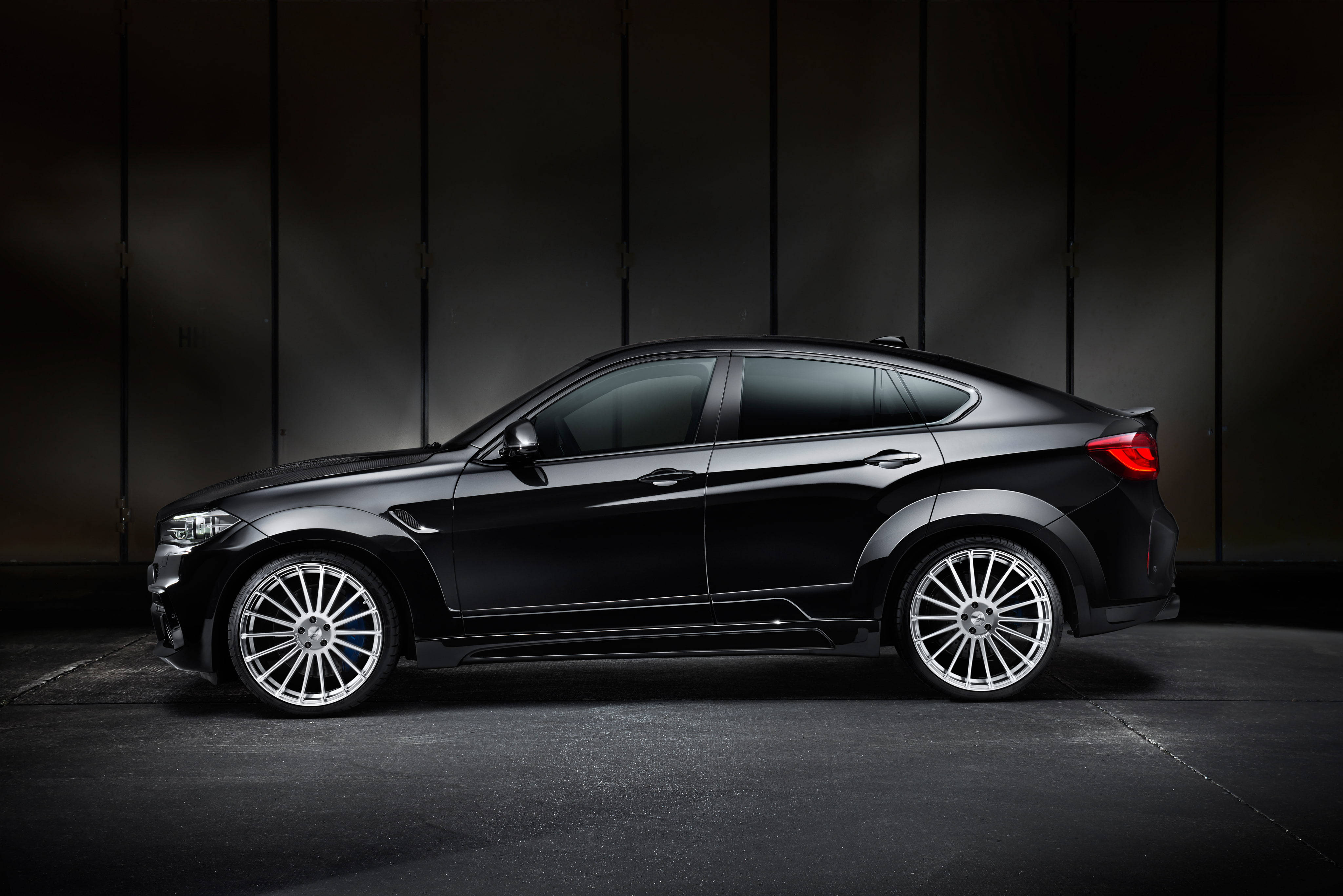 BMW X6 M寬體側面特寫 壁紙 — 一架時尚黑色BMW X6M運動轎跑車配銀色輪圈，矗立在帶有垂直鑲板的昏暗工作室中。