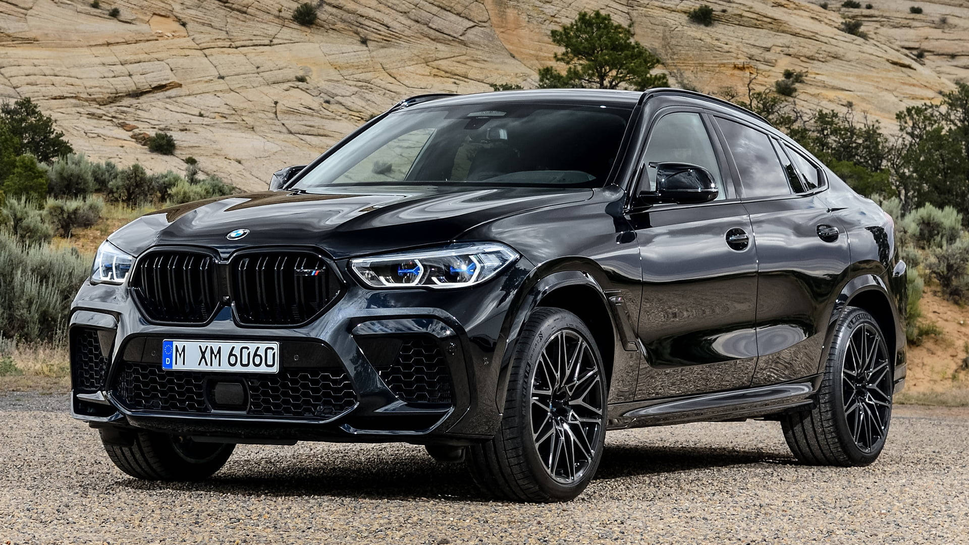 BMW X6 M對比棕色岩層 壁紙 — 一架亮黑色BMW XM 6060 SUV停泊在碎石上，背景係乾旱嘅山丘同稀疏嘅灌木。