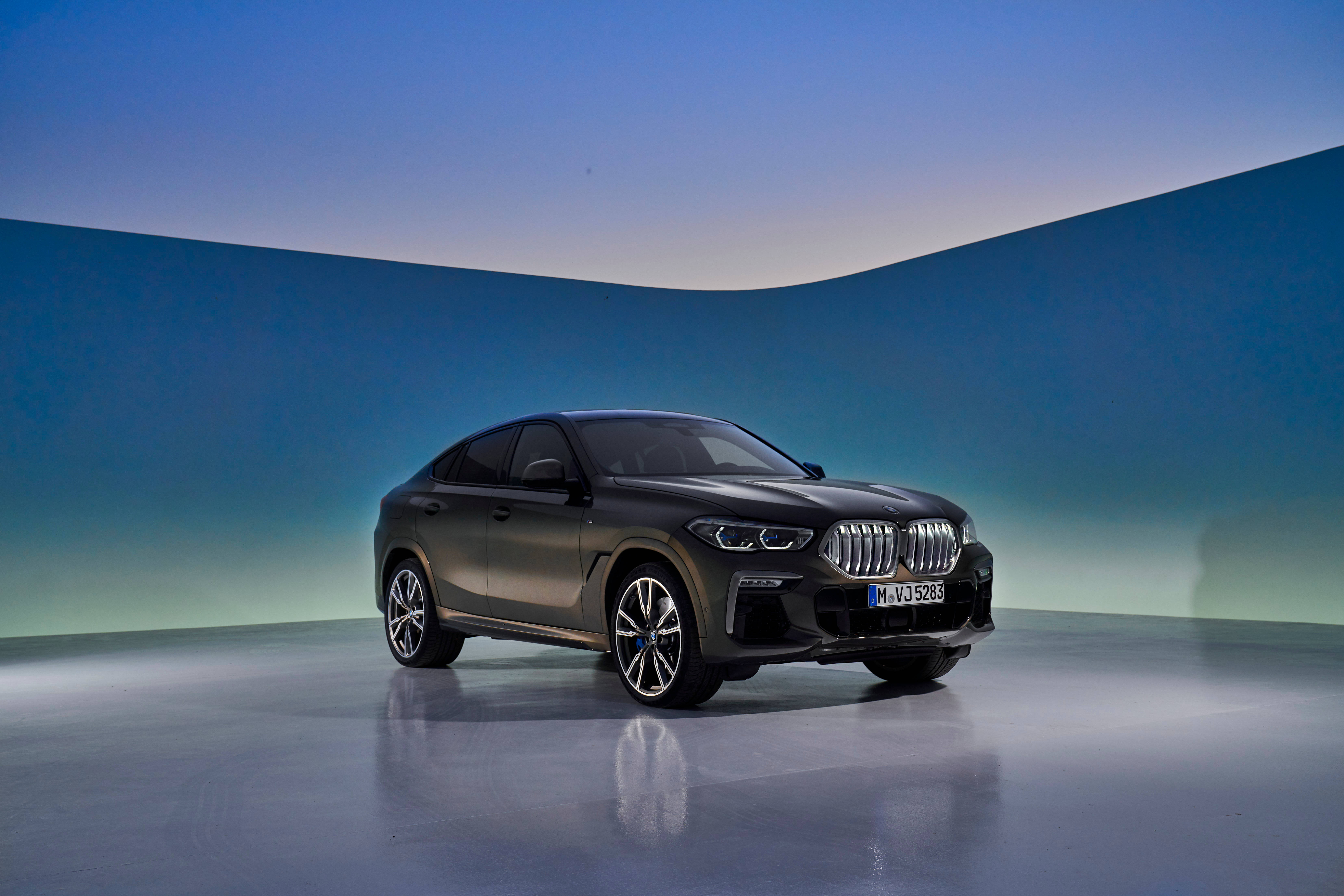 BMW X6 M車型展示 壁紙 — 一輛時尚的啞光黑色BMW X6 SUV在攝影棚燈光下，以漸變藍綠色弧形背景為襯，閃閃發光。