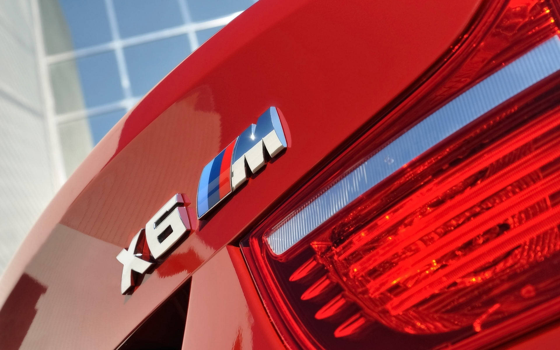 BMW X6 M銀色字樣特寫 壁紙 — 光面紅色BMW X6 M徽章及尾燈反射明亮藍天的特寫。