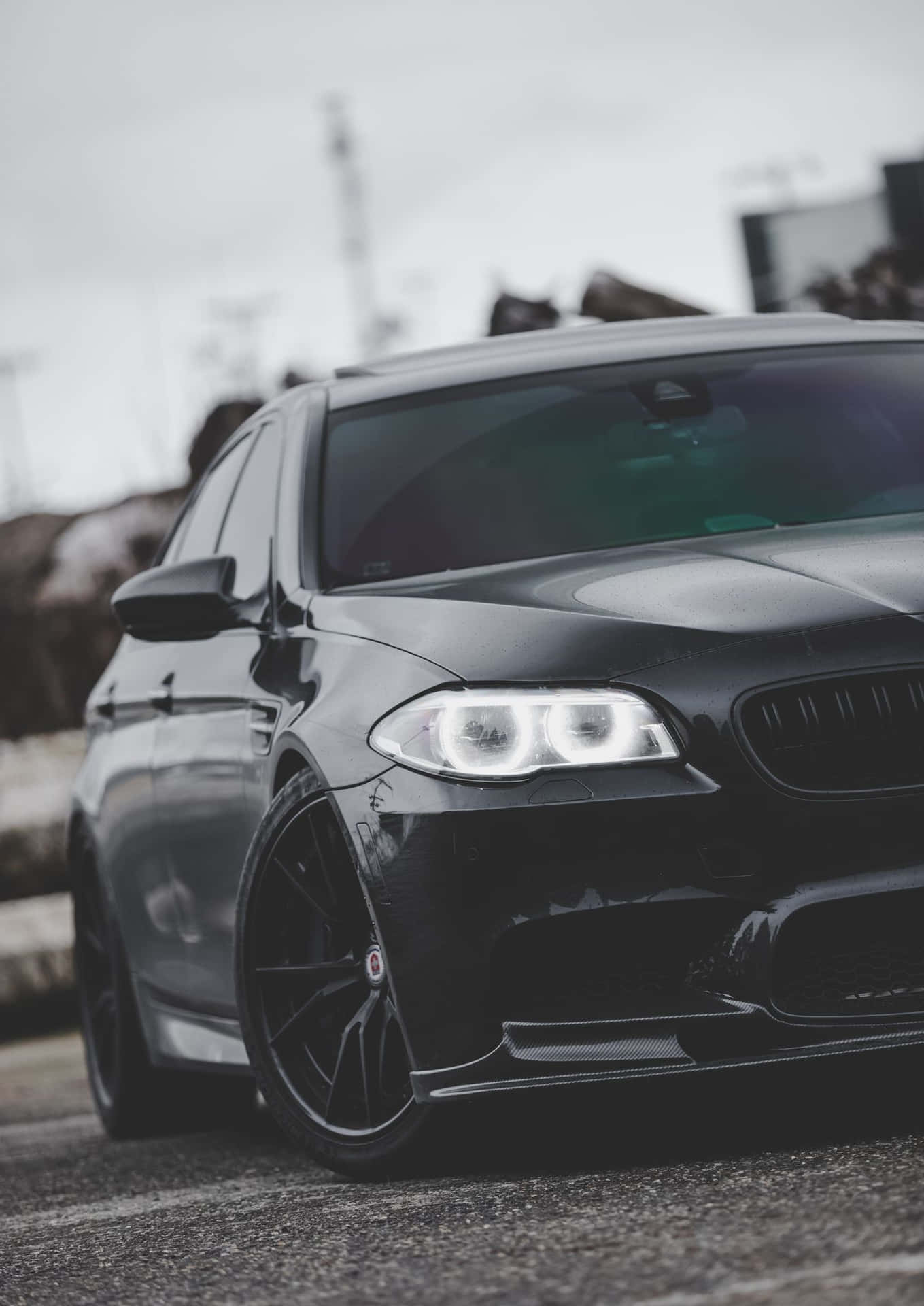 黑色BMW M5跑車，車頭燈明亮，停在瀝青路面上。