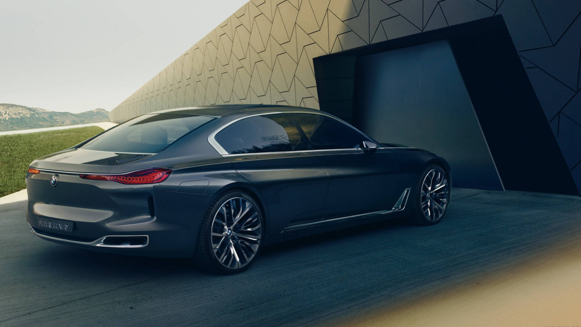 BMW 豪華汽車即將停車 壁紙 — 一輛時尚的深灰色BMW概念車停放在一座現代幾何建築旁邊，背景有山巒。