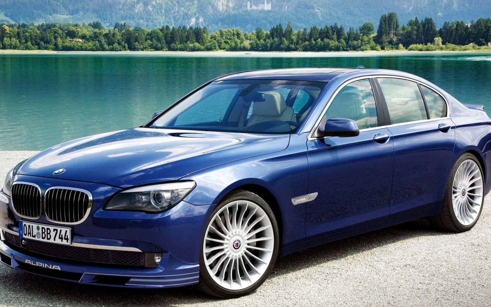 藍色Alpina BMW轎車停泊在風景如畫的湖邊，背景有山脈。