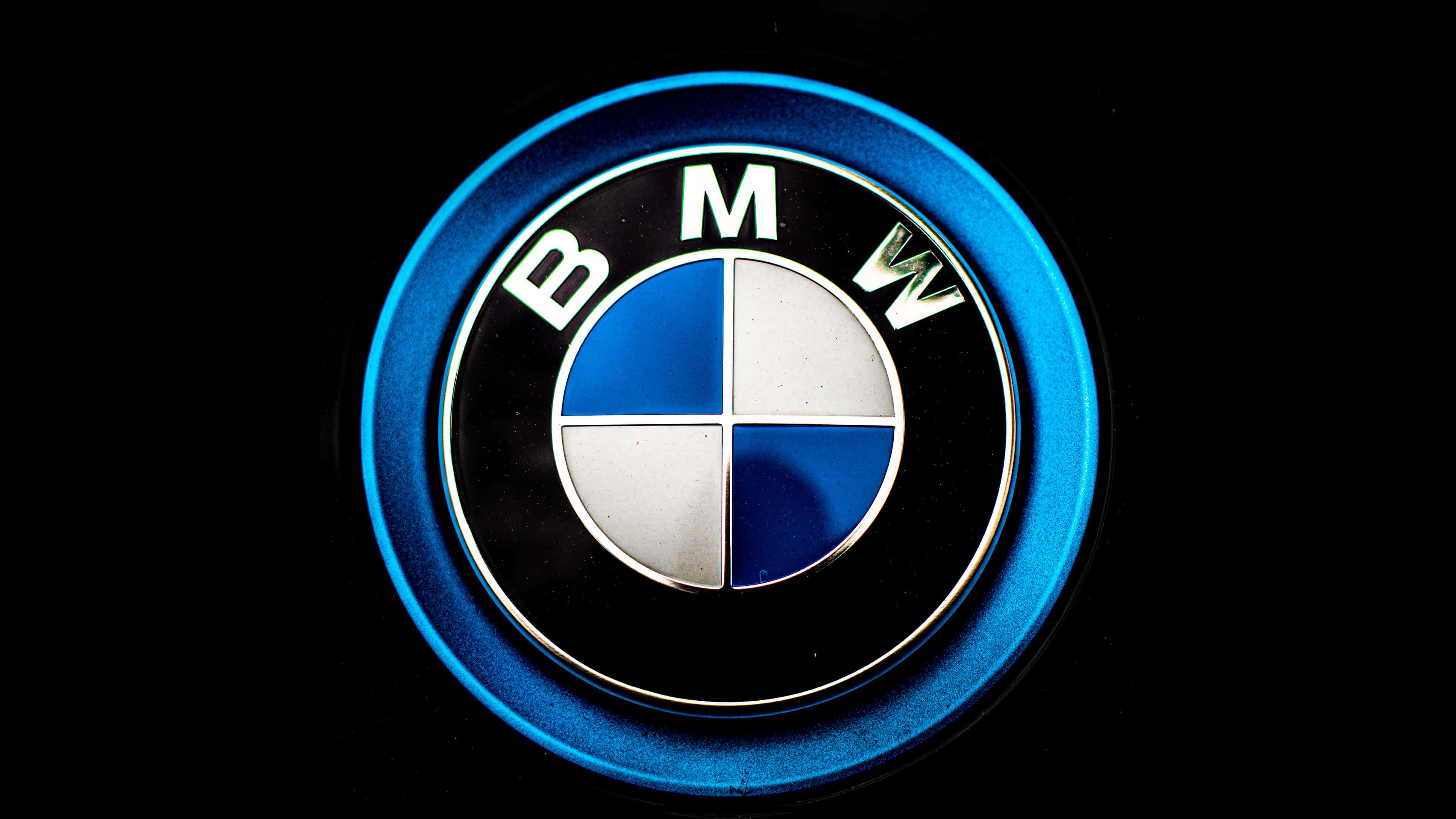 BMW標誌 壁紙 — 黑色背景上帶有金屬光澤的發光藍色BMW標誌徽章的近距離特寫。