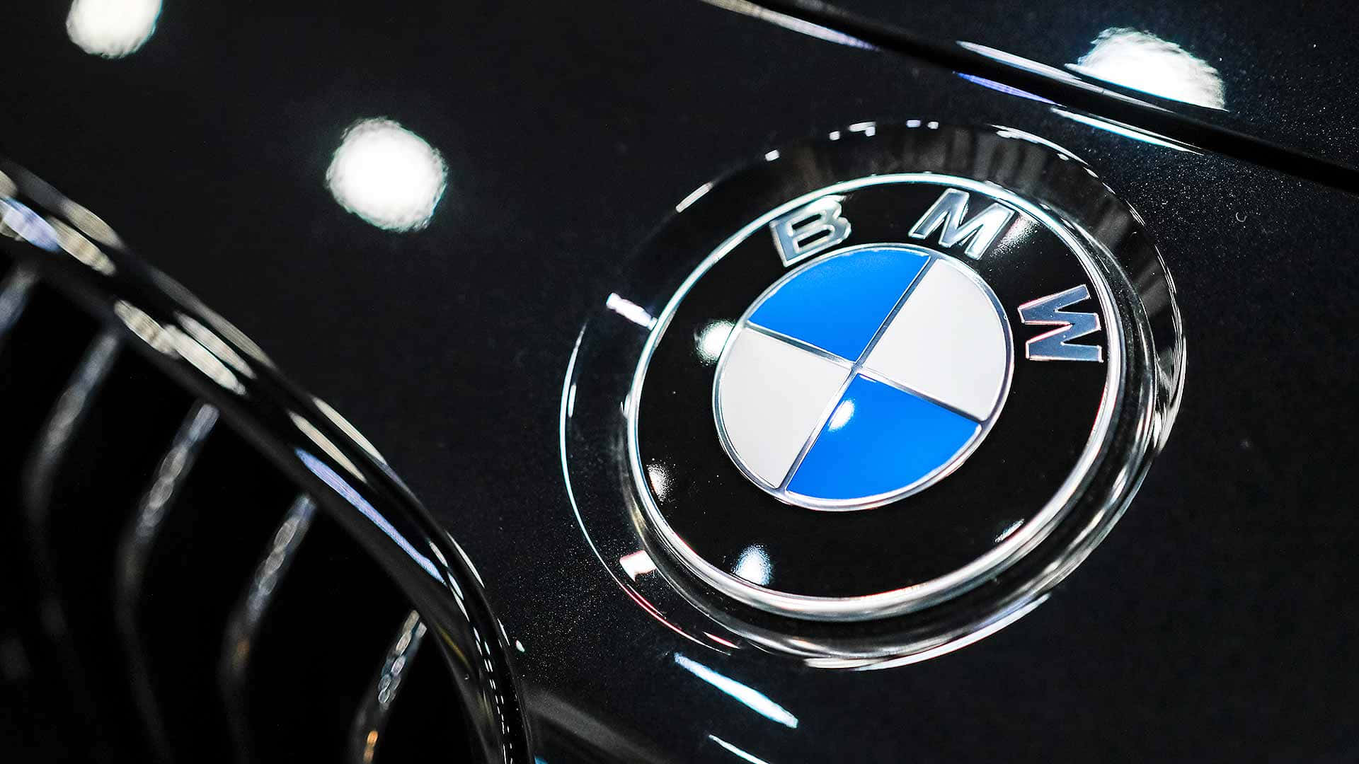 BMW標誌 壁紙 — 黑色光面寶馬汽車引擎蓋的特寫，帶有標誌性的藍白圓形標誌、鍍鉻飾邊和反光。