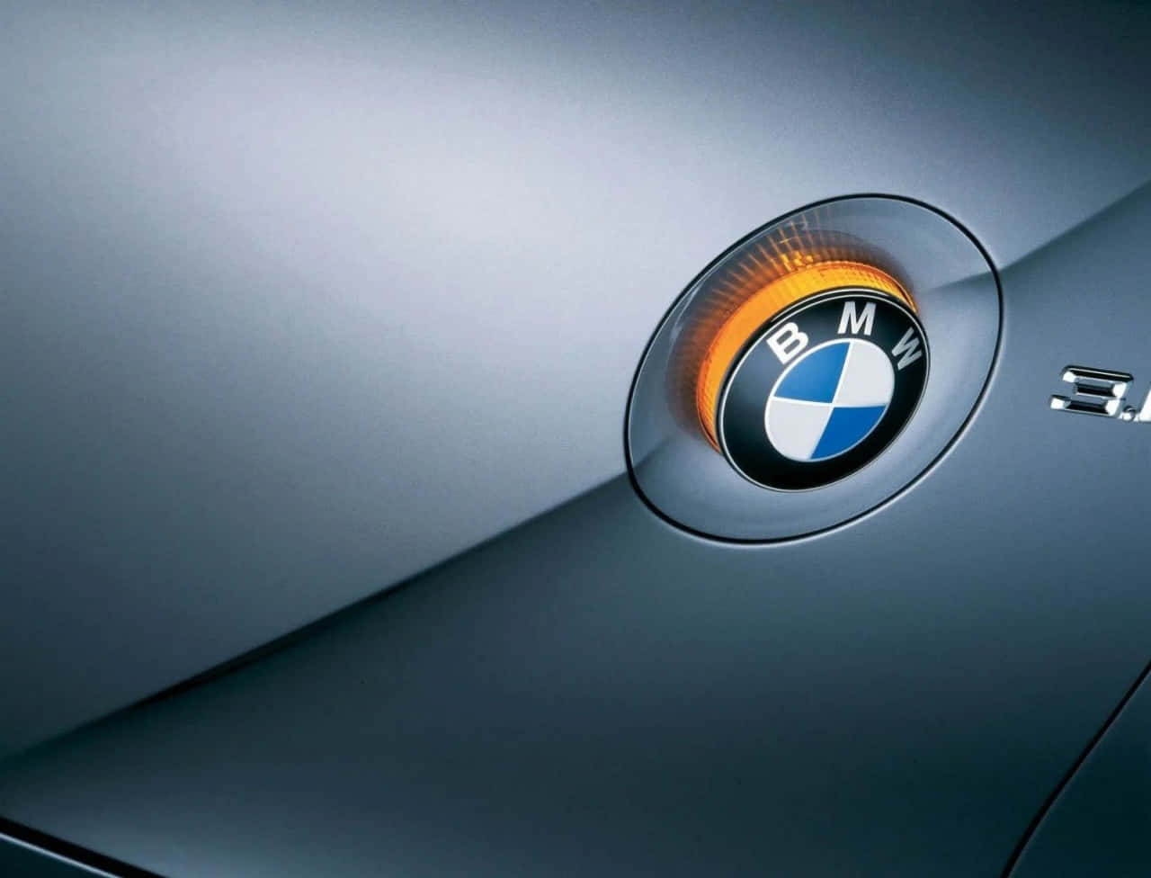 BMW標誌配金屬背景 壁紙 — 寶馬標誌特寫，位於時尚銀色引擎蓋上，帶有發光橙色邊框。
