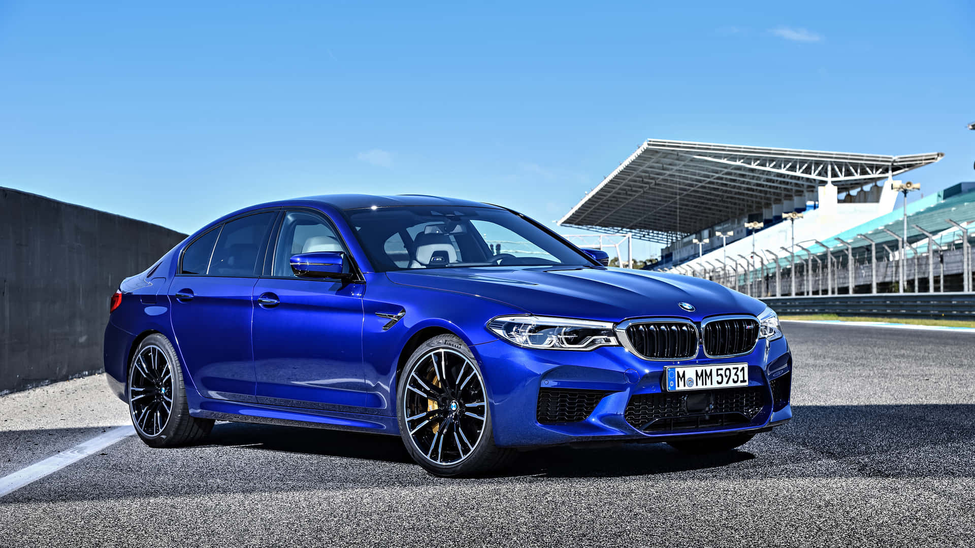 藍色BMW M5轎車在賽道上，背景有看台，天空晴朗。