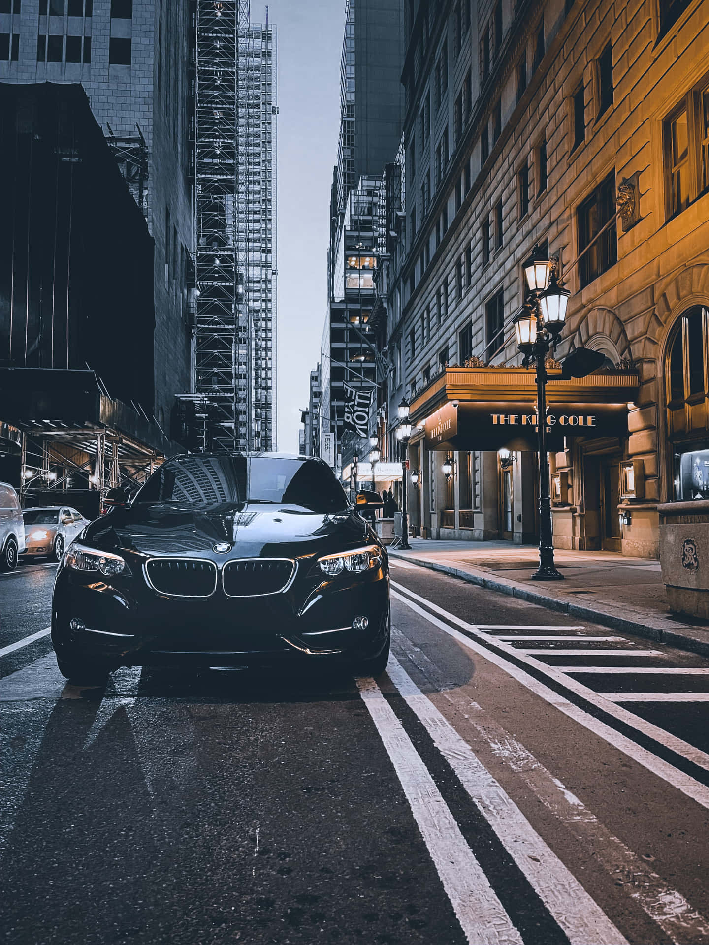 黑色寶馬轎車夜間停在濕漉漉的城市街道上，靠近酒店。