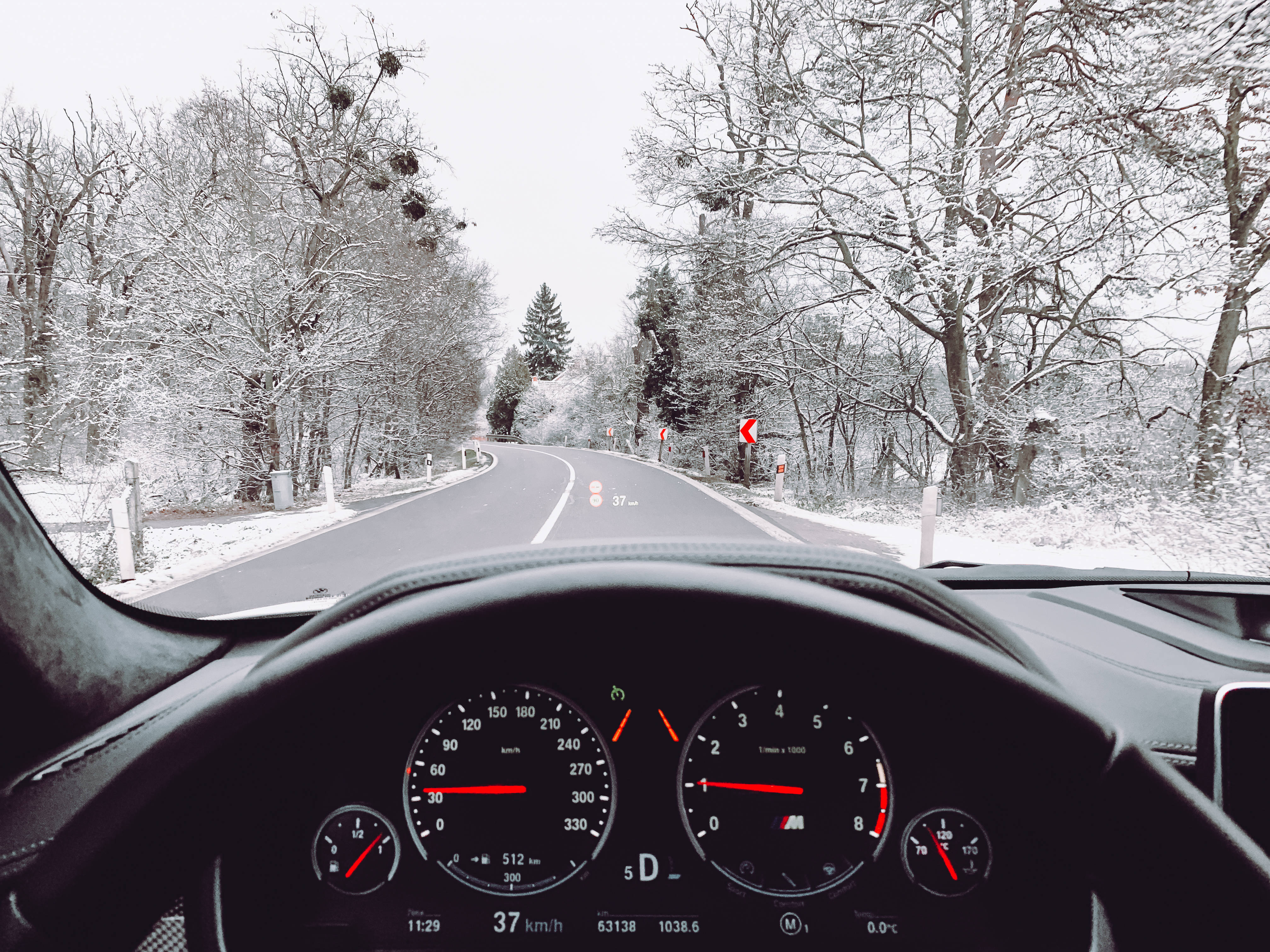 BMW視角冬季桌面 壁紙 — 穿過白雪覆蓋的森林道路，兩旁是光禿禿的樹木，前方是蜿蜒的瀝青路。