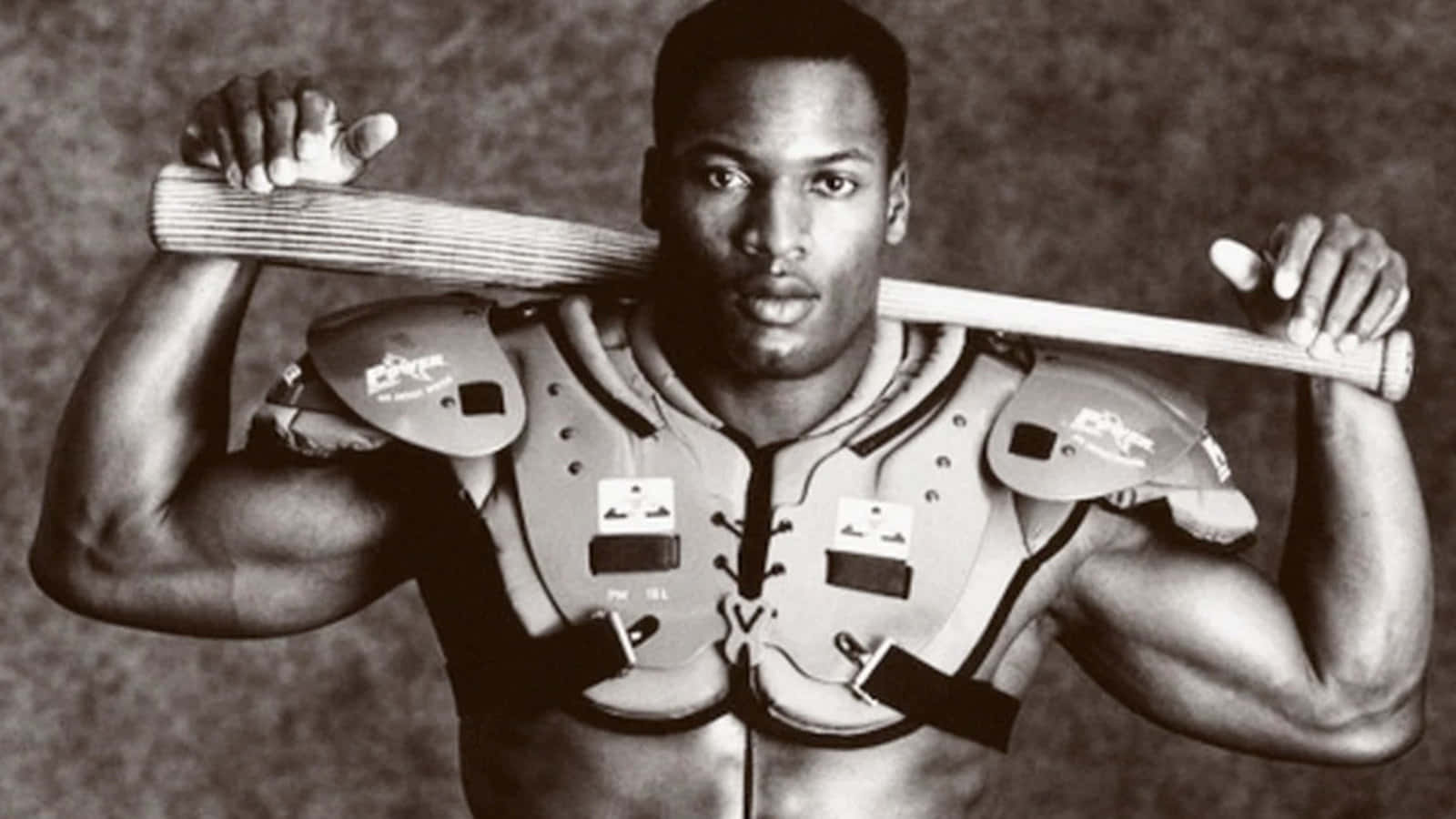 Bo Jackson 身穿足球背心 壁紙 — 一位肌肉發達的足球運動員穿著肩墊，在鮮明的黑白工作室肖像中將球棒扛在肩上。