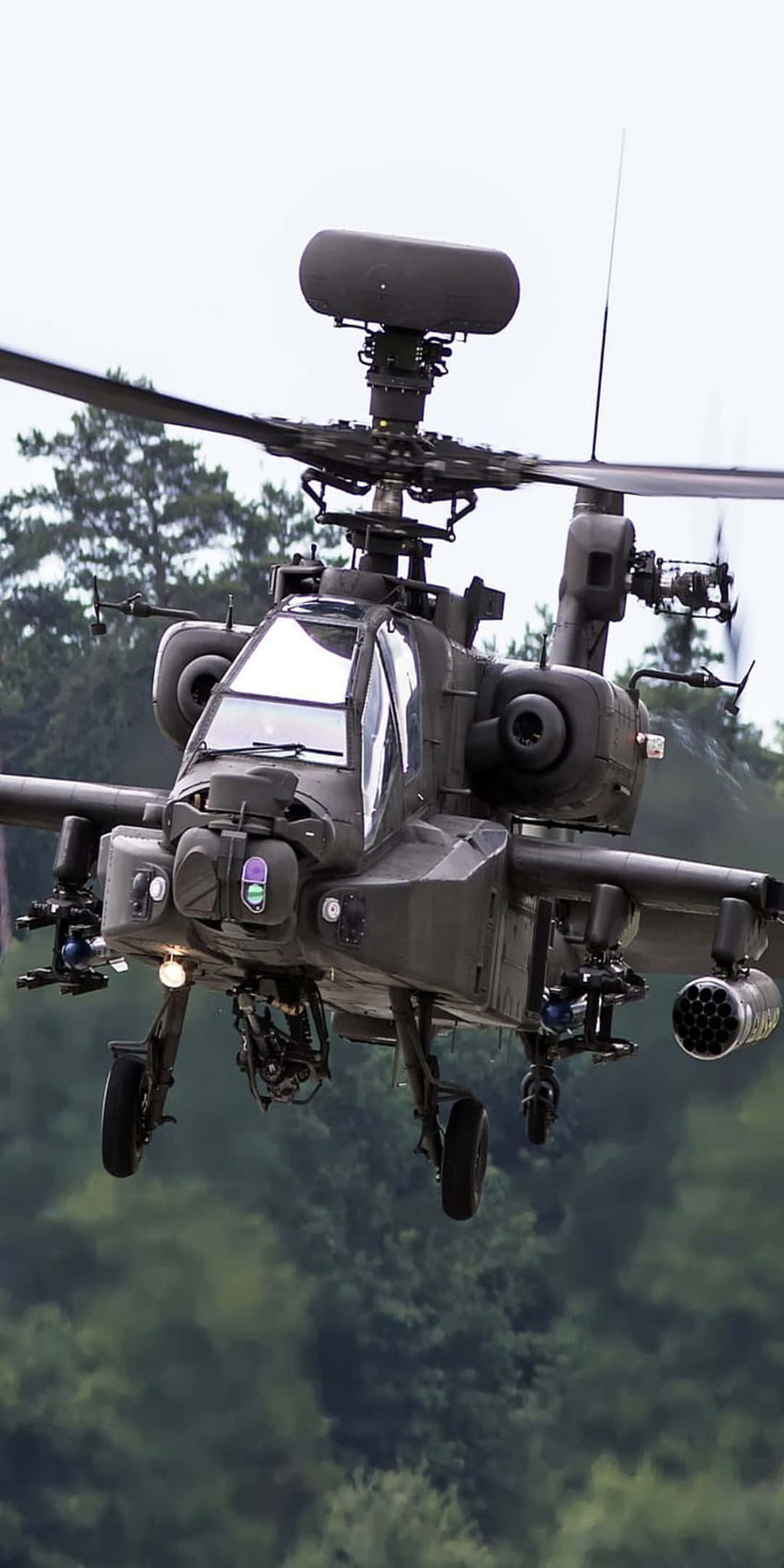 Boeing AH-64 Apache直升機 - Pixel 3背景 壁紙 — 一架軍用攻擊直升機在陰天低空盤旋於茂密的綠色森林樹冠之上。