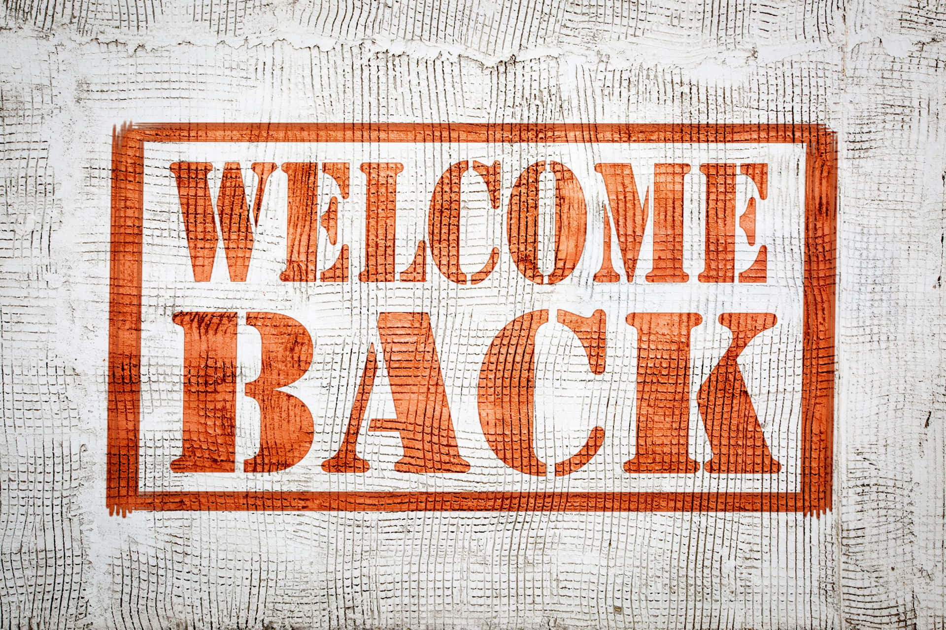 壁紙 — 在風化的白色木紋上，一個破舊框架內有醒目的橙色「WELCOME BACK」文字。