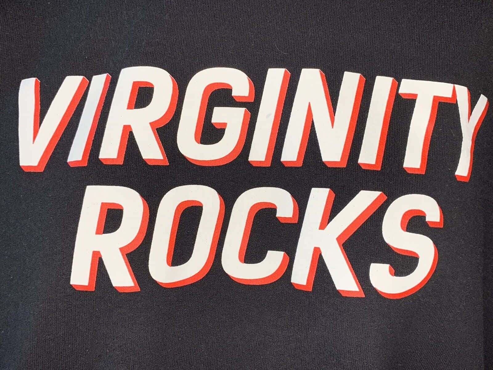  壁紙 — 深色布料上大膽的白色和橙色「VIRGINITY ROCKS」文字，可見針織紋理。