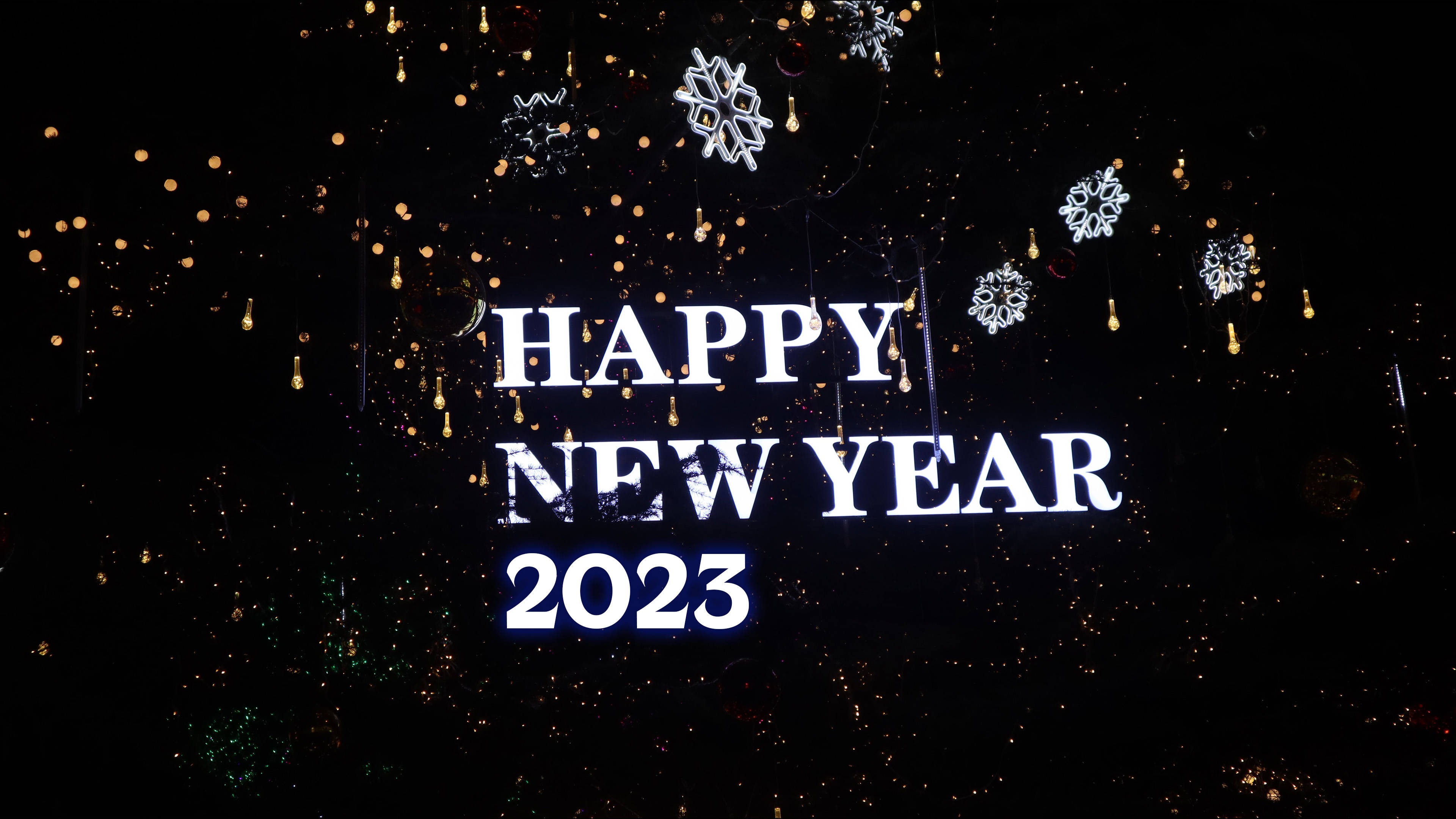 Happy New Year 2023 發光標誌，帶有懸掛的雪花和夜晚閃爍的燈光。