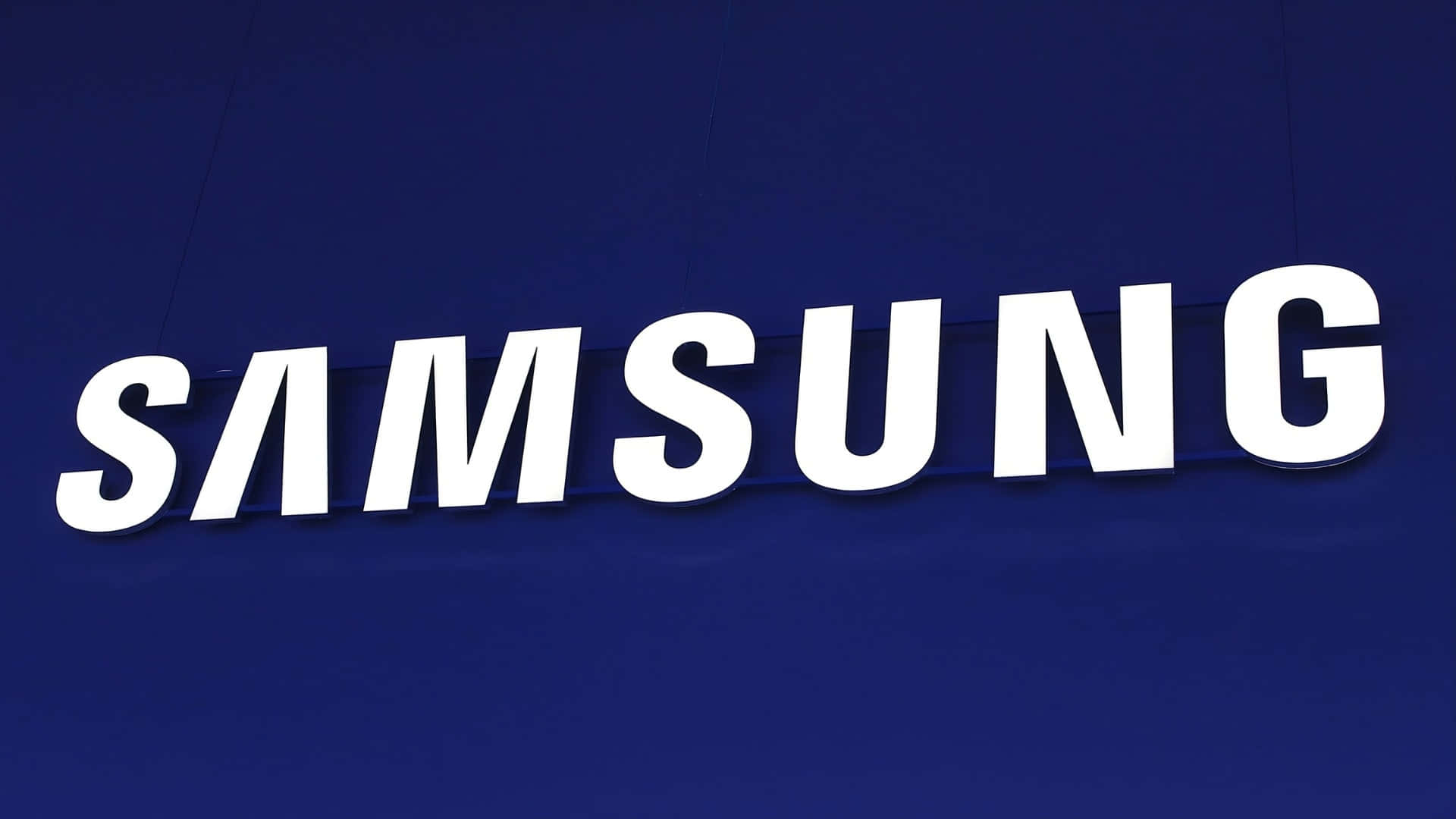  壁紙 — 大膽的白色Samsung標誌在深藍色紋理牆壁上脫穎而出，營造出乾淨的企業環境。