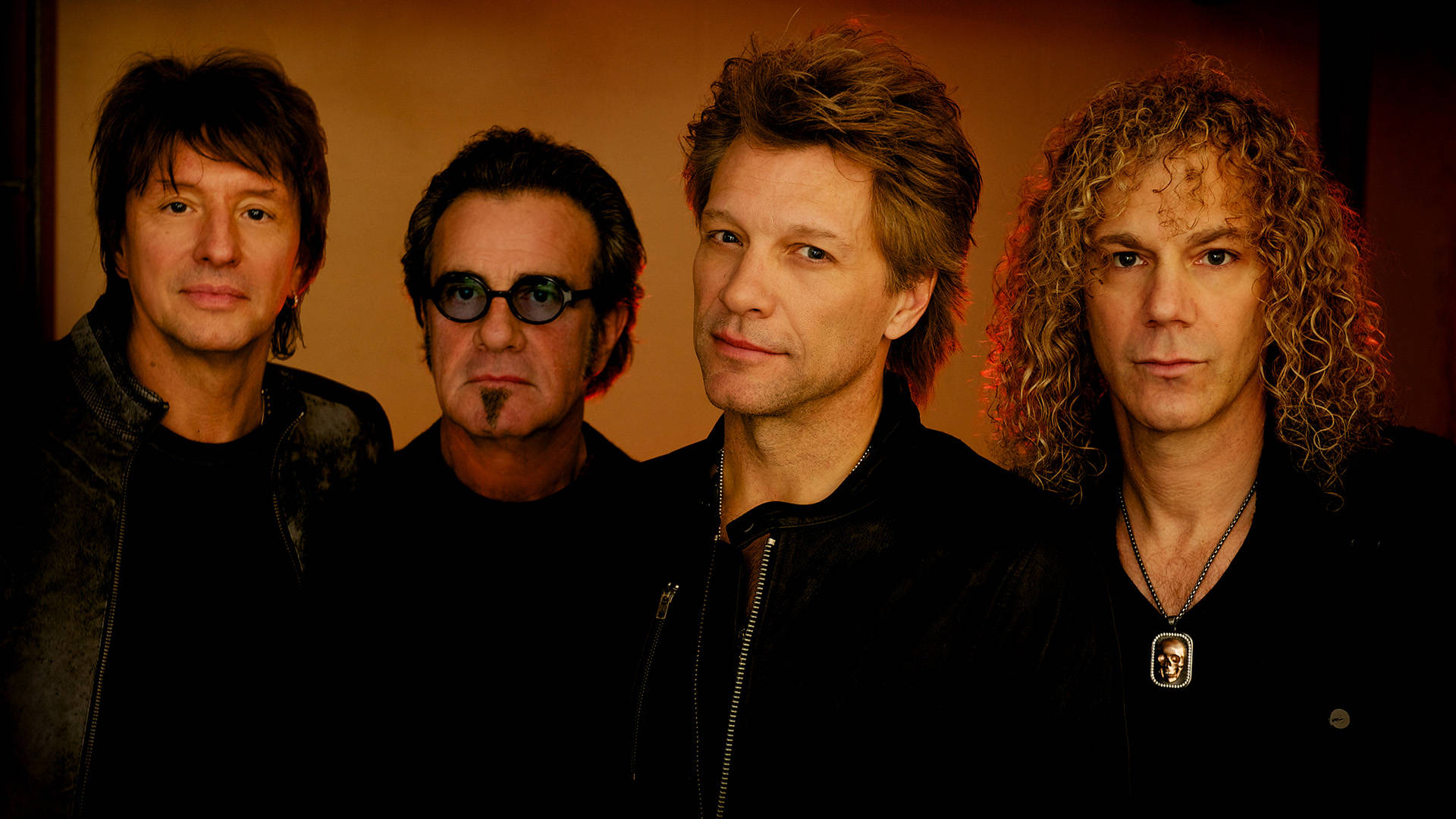 美國搖滾樂團Bon Jovi David Bergman攝影肖像 壁紙 — 四位髮型各異、身穿深色衣服的男子，在暖色調的攝影棚背景前嚴肅地擺姿勢。