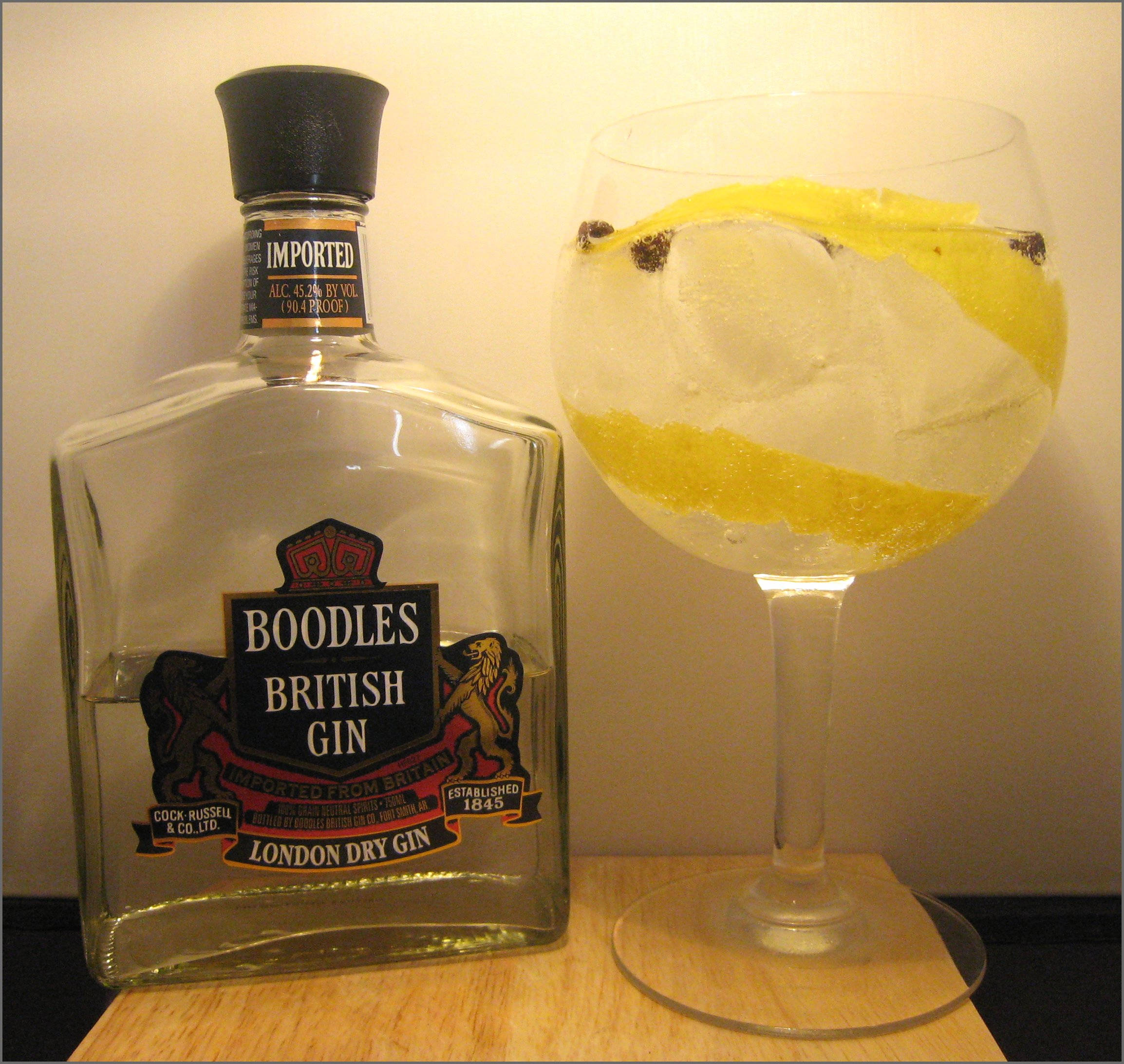 Boodles 1970年代瓶身設計 壁紙 — 一瓶Boodles British Gin放在木質表面上，旁邊是一杯以檸檬和橄欖裝飾的氈酒湯力。