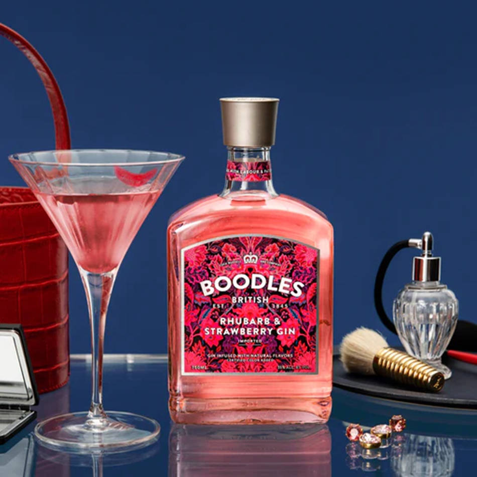 Boodles 草莓與薔薇酒 壁紙 — 一個充滿活力的粉紅色大黃草莓氈酒瓶，旁邊放著一杯相配的馬提尼酒杯中的雞尾酒，置於反光表面上。