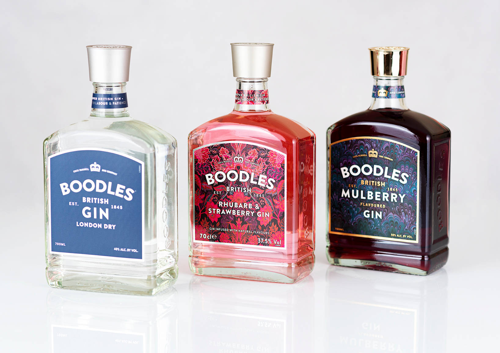 Boodles最佳金酒品牌 壁紙 — 三瓶透明粉紅和深紫色調的Boodles氈酒瓶，立於反光的白色表面上，背景為純淨的白色。