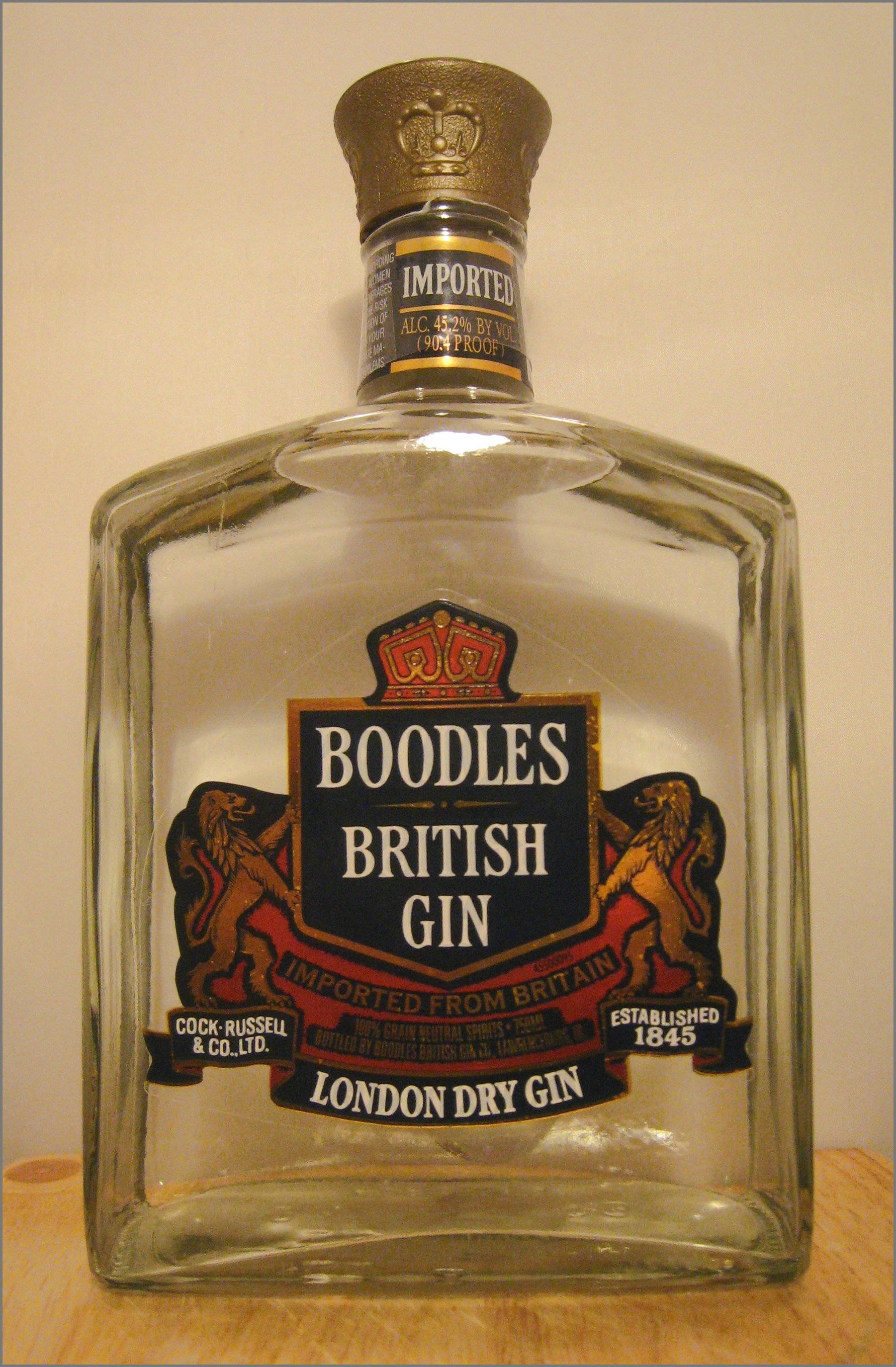 Boodles絕佳收藏瓶 壁紙 — 一個透明玻璃瓶的Boodles British Gin，帶有金色瓶蓋和裝飾有獅子與皇冠的華麗標籤，放置在木質表面上。