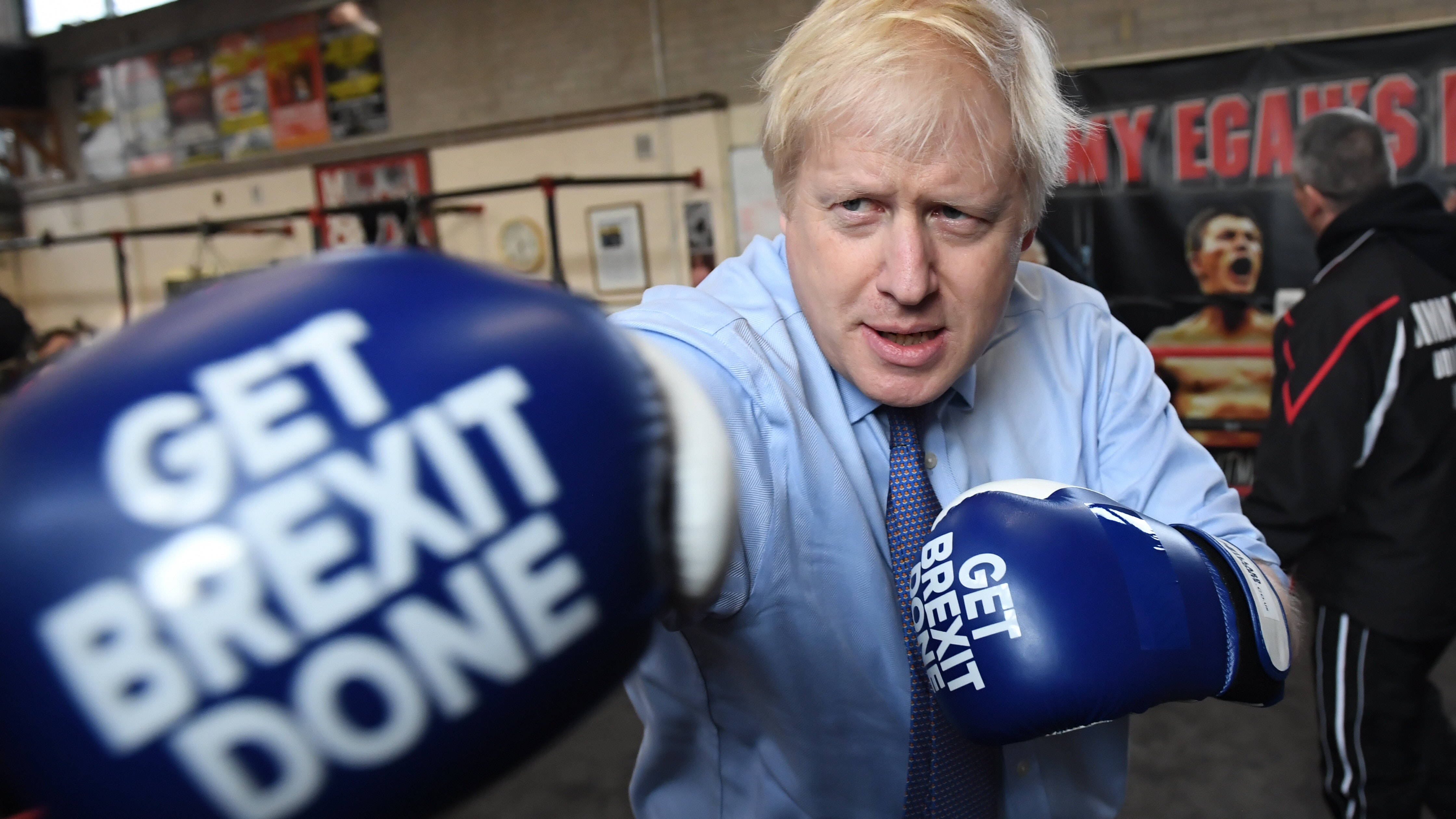 Boris Johnson 拿著訊息 壁紙 — Boris Johnson 在拳擊健身室戴上藍色手套，帶有「GET BREXIT DONE」字樣，擺姿勢拍照。