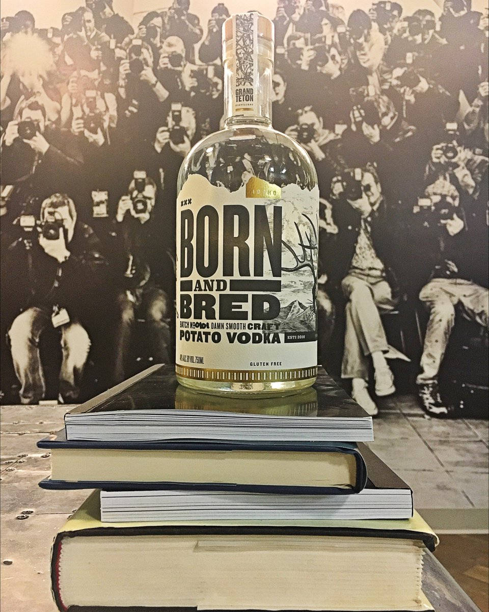 Born And Bred書籍堆疊 壁紙 — 一瓶清澈的 Born and Bred 馬鈴薯伏特加放在一堆書本上，背景是攝影師的黑白照片。