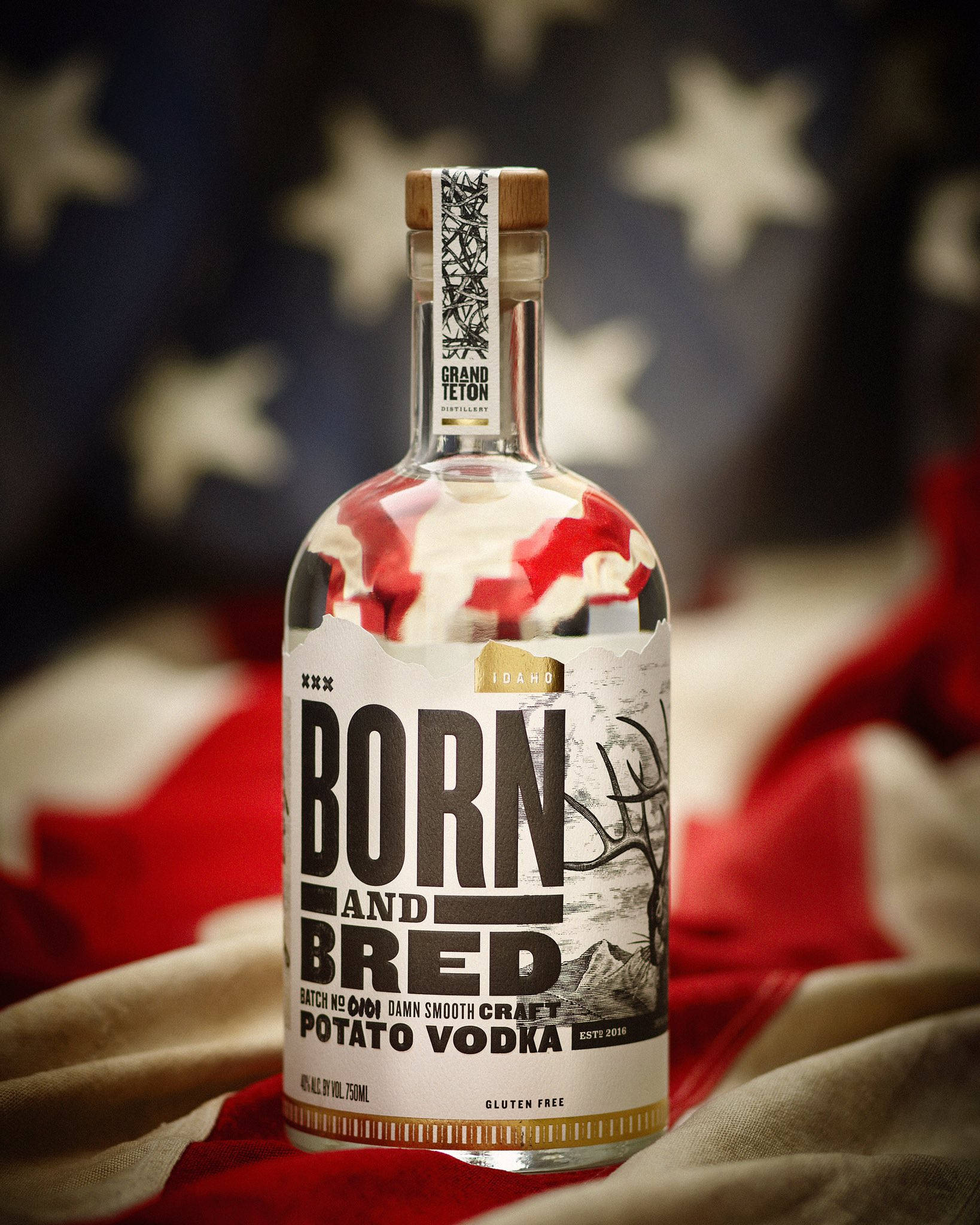 Born And Bred美國國旗布 壁紙 — 一瓶清澈的Born and Bred馬鈴薯伏特加酒，醒目地放在模糊的美國國旗背景前。