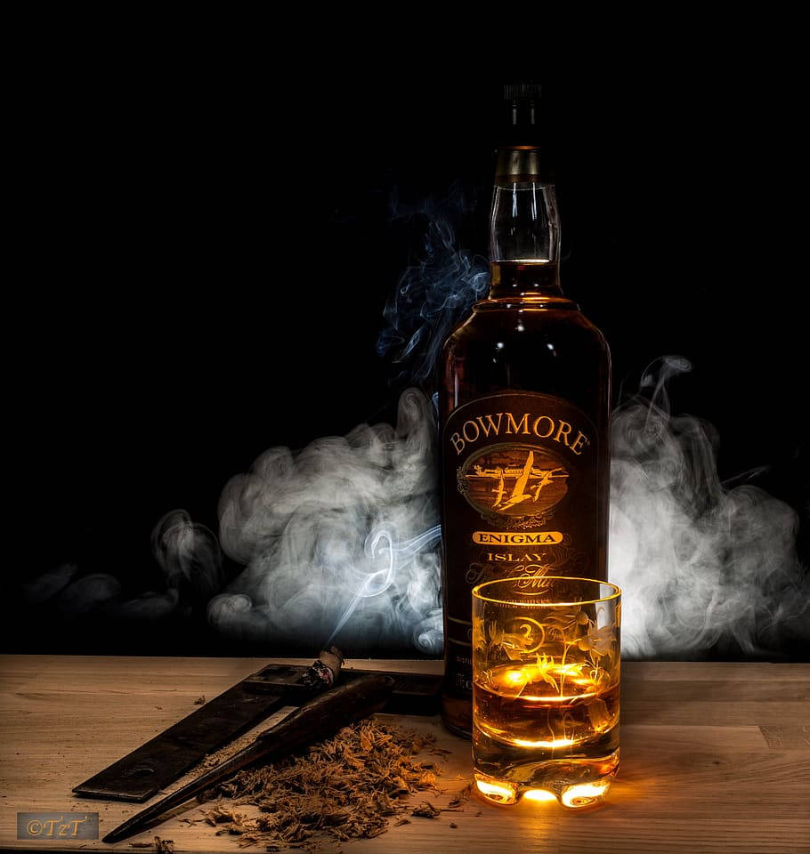 Bowmore 威士忌瓶和酒杯，帶有煙霧和雪茄剪在木桌上。