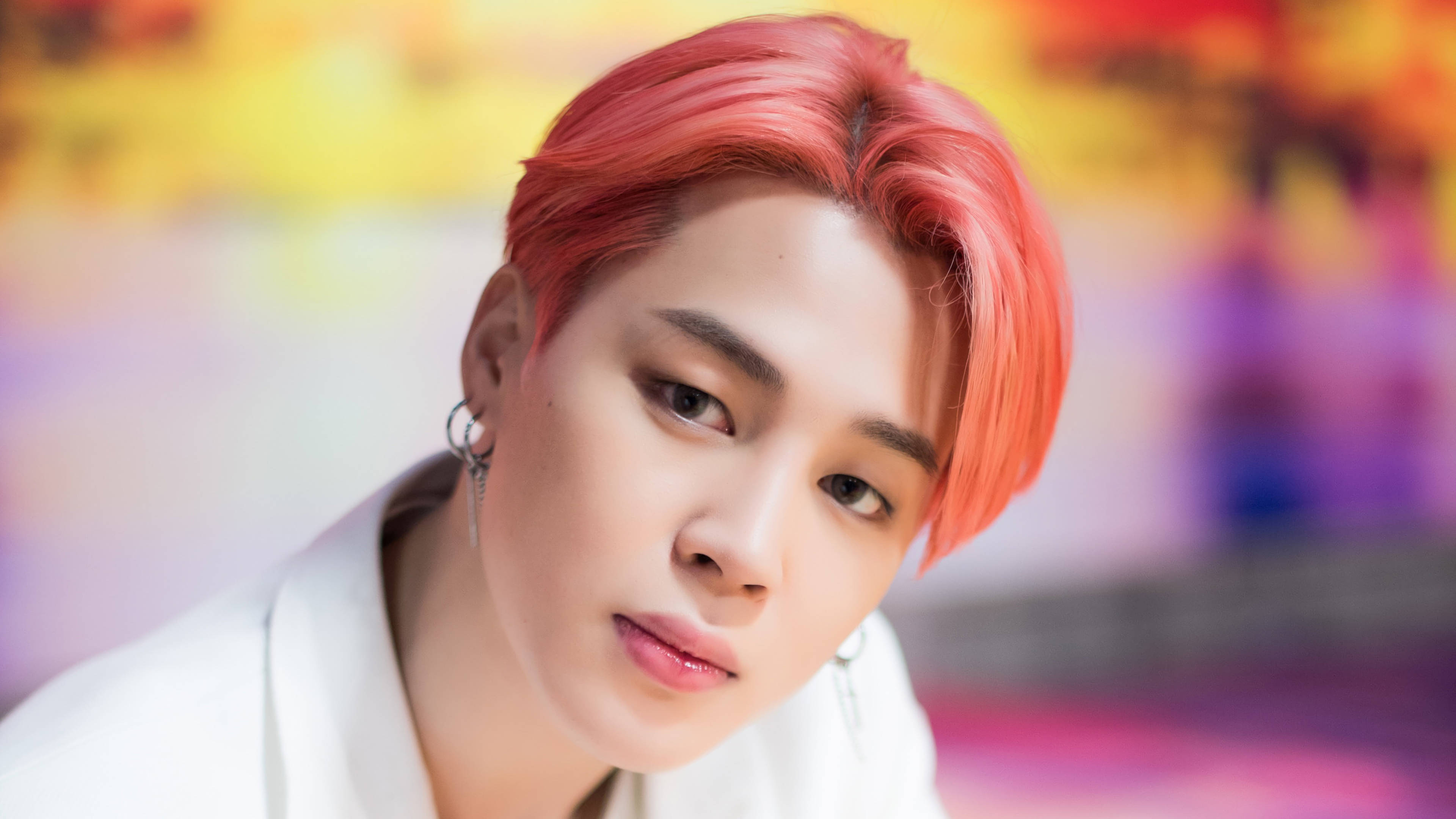 Boy With Luv 朴智旻 壁紙 — 一個擁有鮮豔紅髮和銀色耳環的人，在色彩繽紛的模糊背景下直視鏡頭。