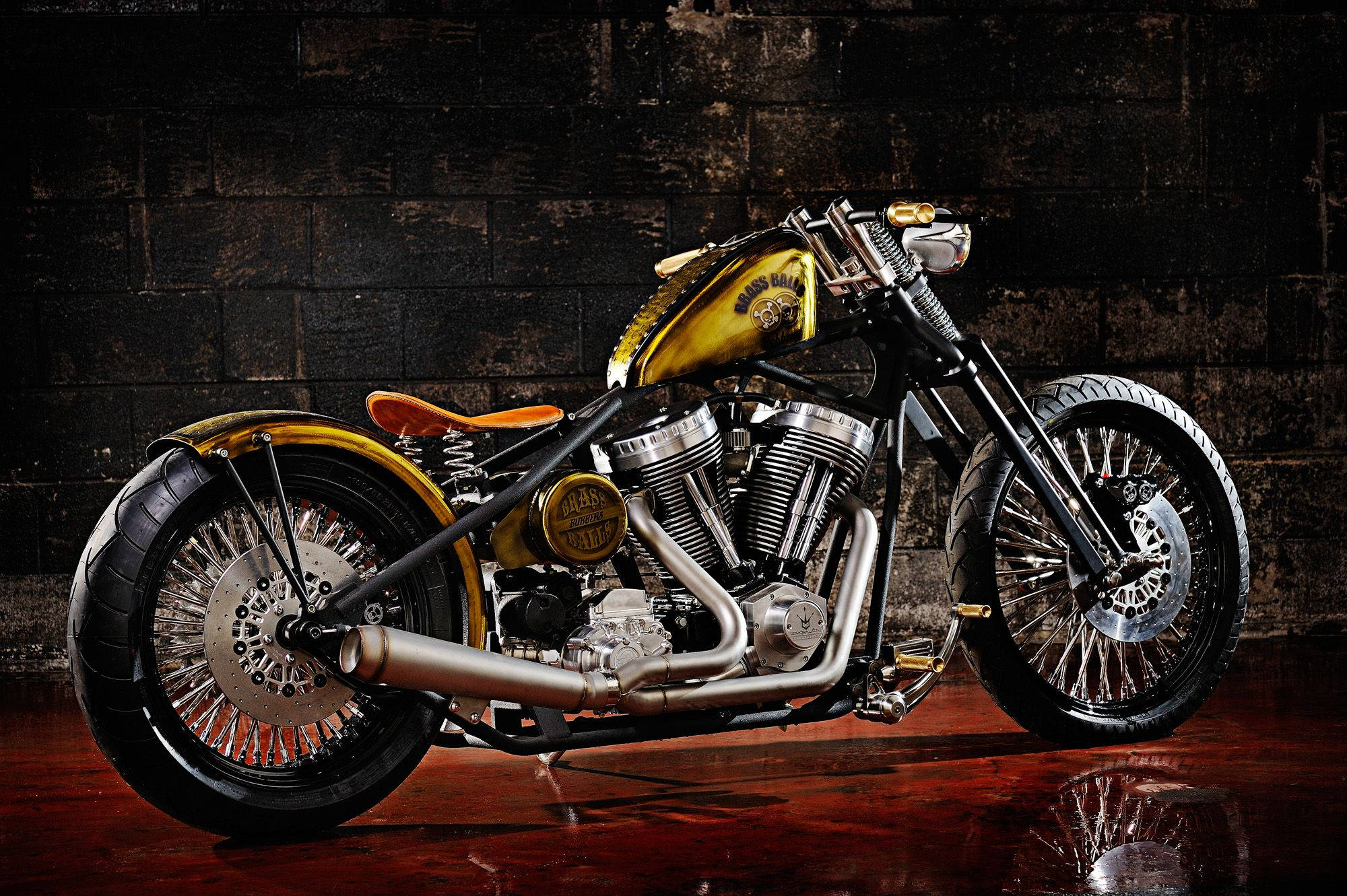 Brass Balls Cycles 哈雷摩托車 壁紙 — 一架訂製嘅chopper電單車，帶有金色點綴同鉻金屬細節，喺深色磚牆前嘅反光木地板上戲劇性地展示。