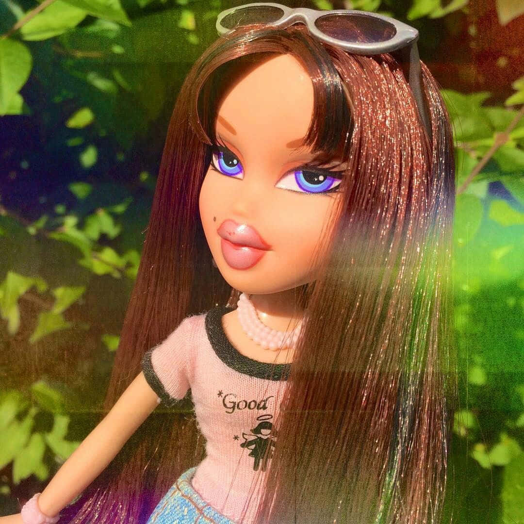 釋放你內在的Bratz時尚達人！ 壁紙 — 一個 Bratz 公仔，擁有長長的閃亮頭髮和藍色眼睛，在戶外擺姿勢，頭上戴著太陽眼鏡，背景是茂密的綠色樹葉。