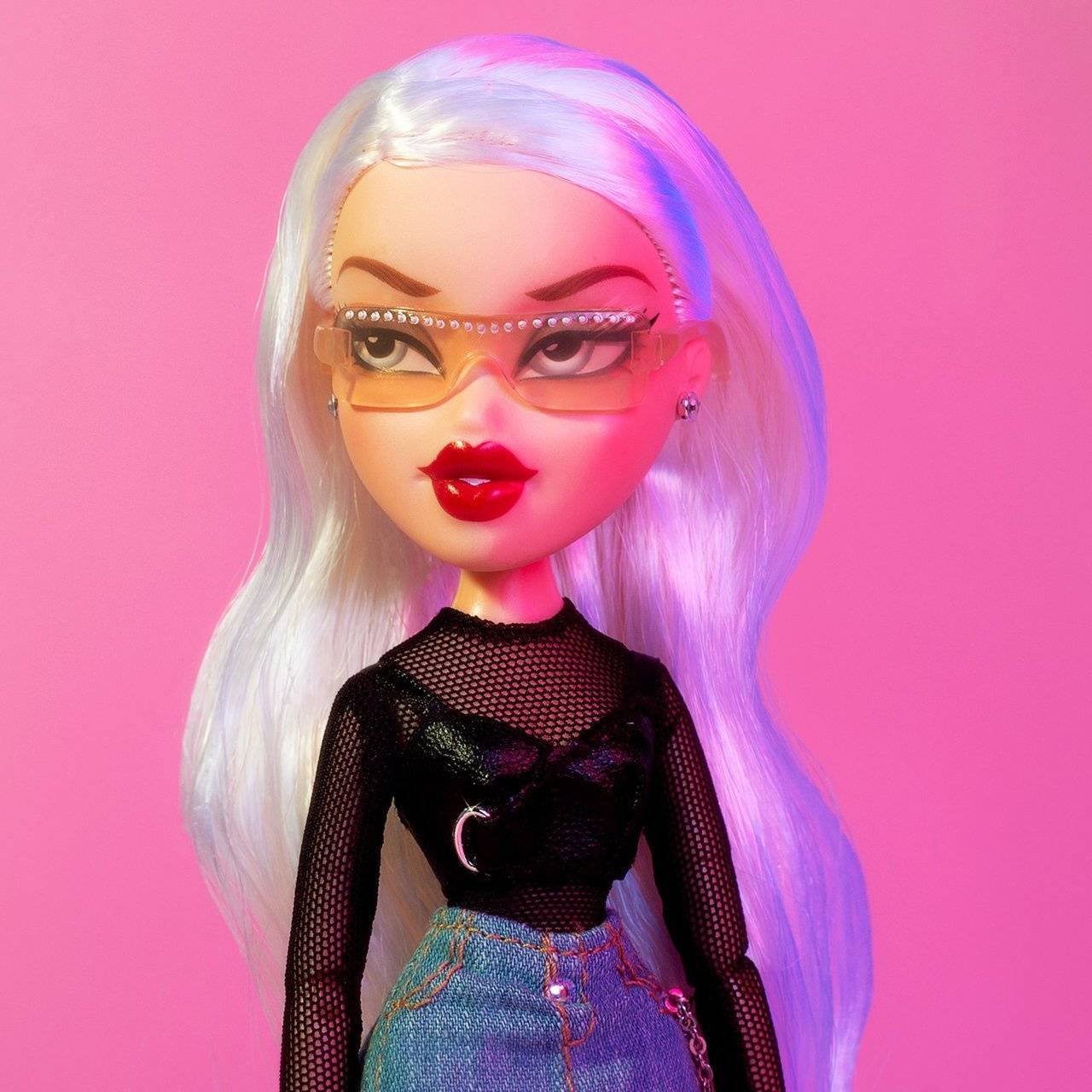 Bratz娃娃Cloe肖像照 壁紙 — 一個擁有鉑金色頭髮和大膽紅唇的玩偶，在充滿活力的粉紅色背景下戴著超大眼鏡。