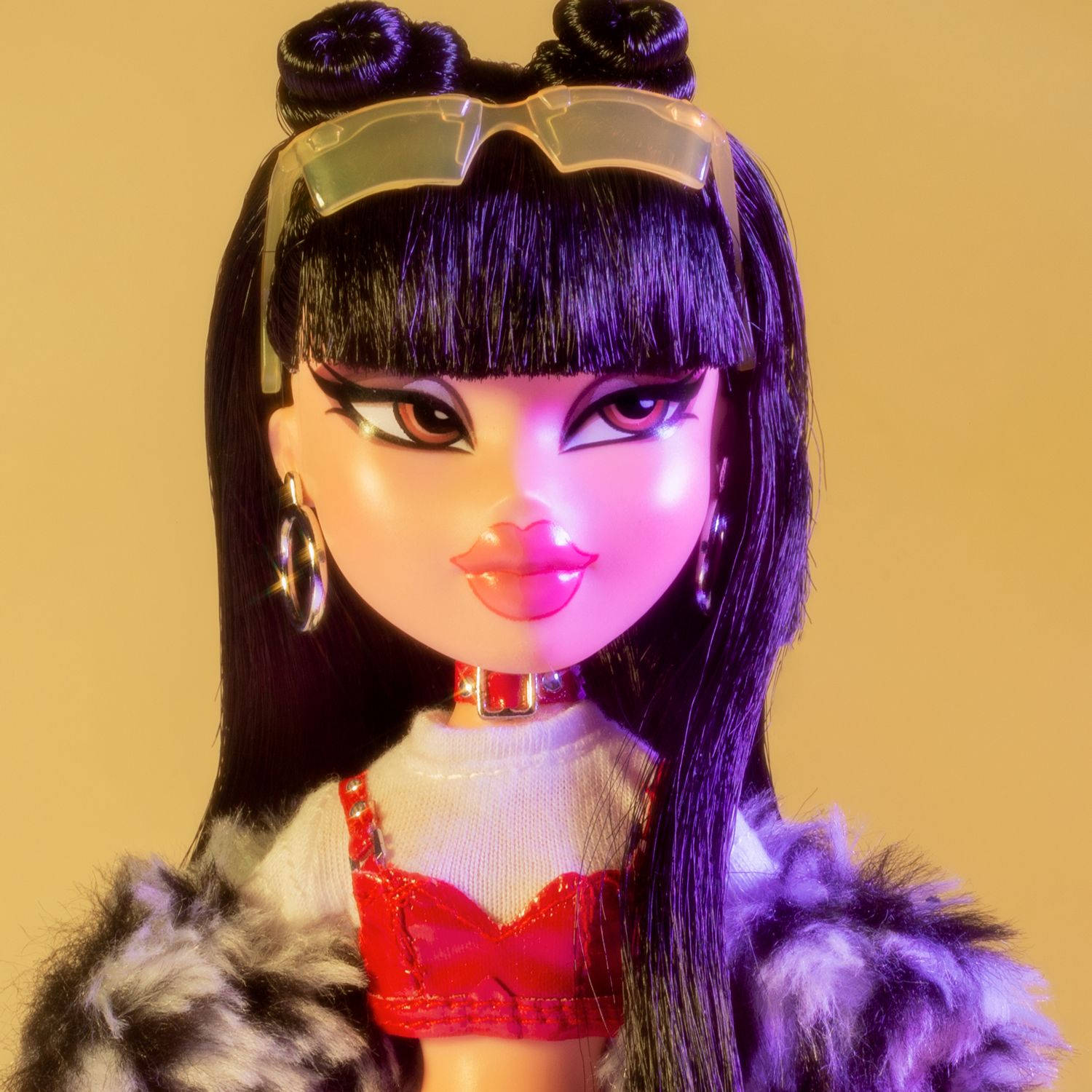 Bratz娃娃Jade雙馬尾造型 壁紙 — 一個紫色頭髮、戴著未來感眼鏡的娃娃，在溫暖的黃色背景前擺姿勢，身穿紅色上衣和毛皮外套。