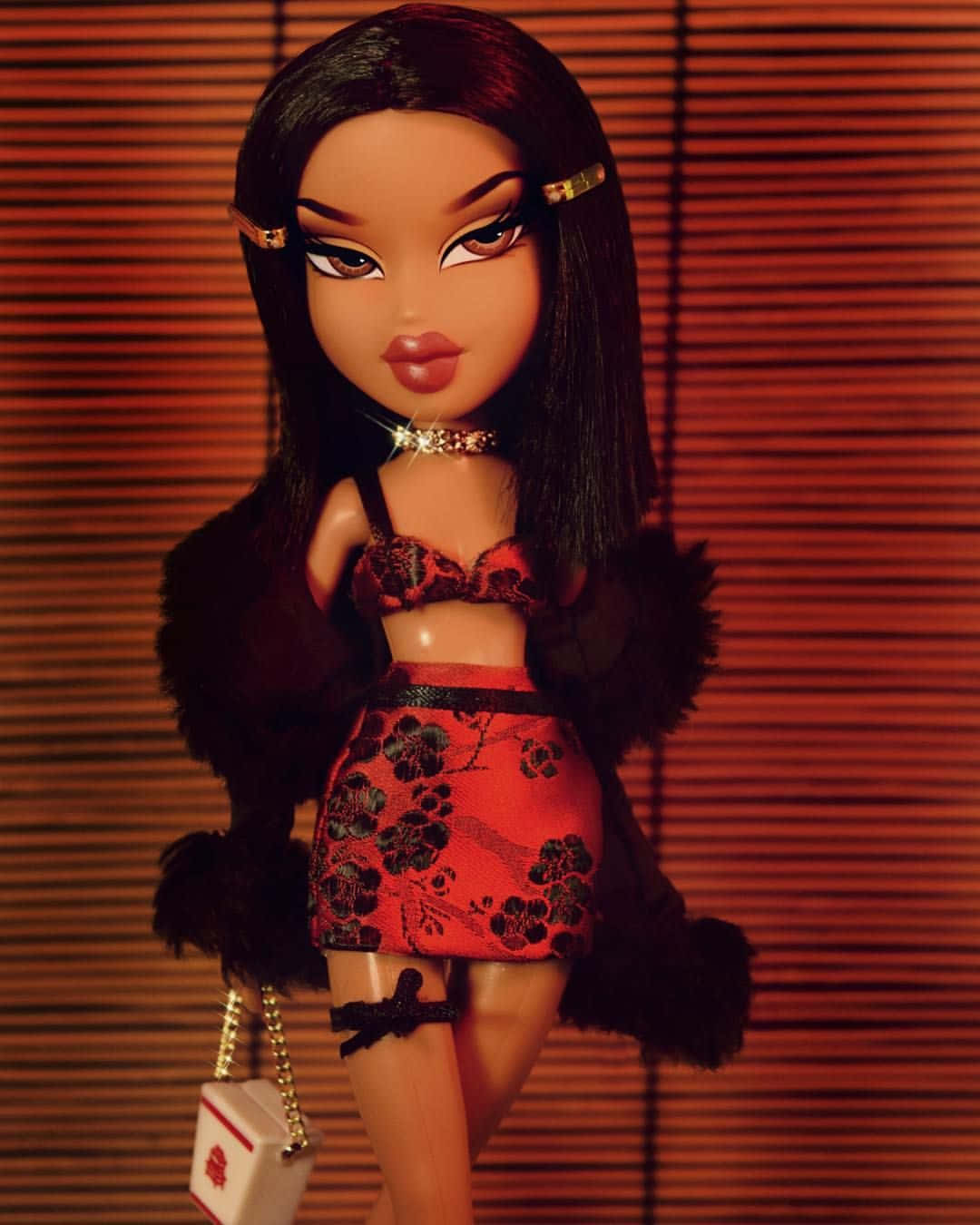 Bratz娃娃美學的迷人視覺 壁紙 — 一個 Bratz 公仔穿著紅色花卉服裝和黑色毛皮披肩，在溫暖的木百葉窗前拿著時尚手袋擺姿勢。