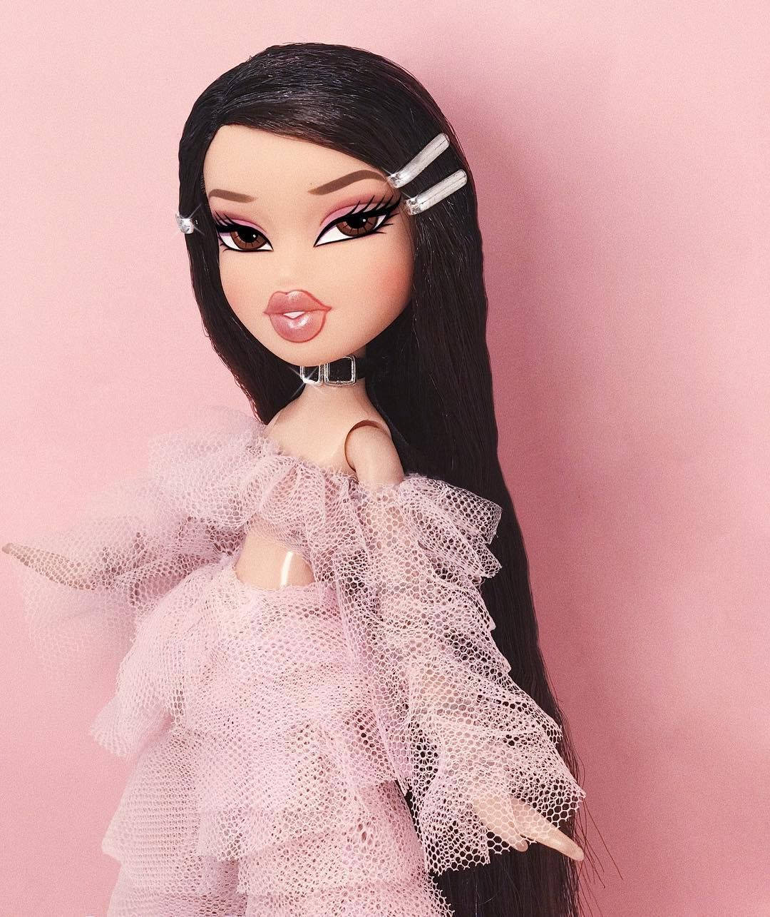 Bratz玩偶粉紅拍攝 壁紙 — 一個 Bratz 娃娃，長長的黑髮和銀色髮夾，穿著多層粉紅色薄紗服裝，背景是柔和的粉紅色。