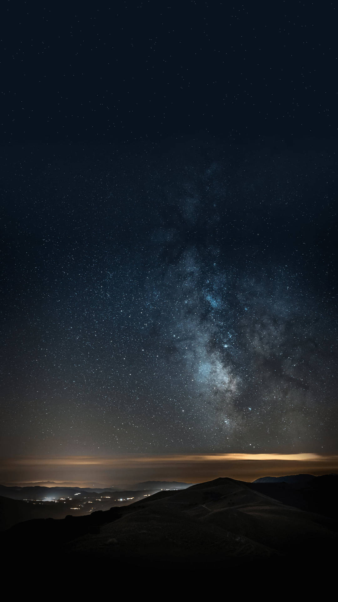 銀河系在黑暗的山脈和遠處的城市燈光上方的星空夜空中延伸。