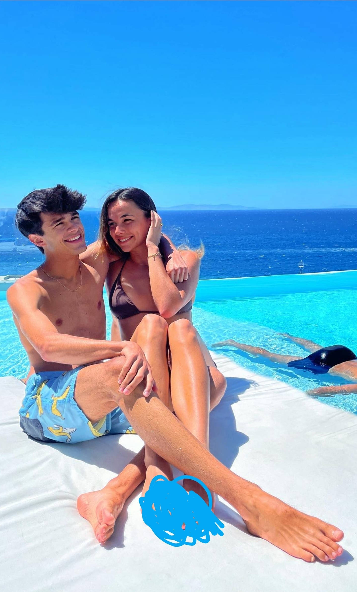 Brent Rivera 與 Lexi Rivera 海景合照 壁紙 — 一對微笑的情侶在無邊際泳池旁休息，俯瞰著晴朗天空下廣闊的藍色海洋。