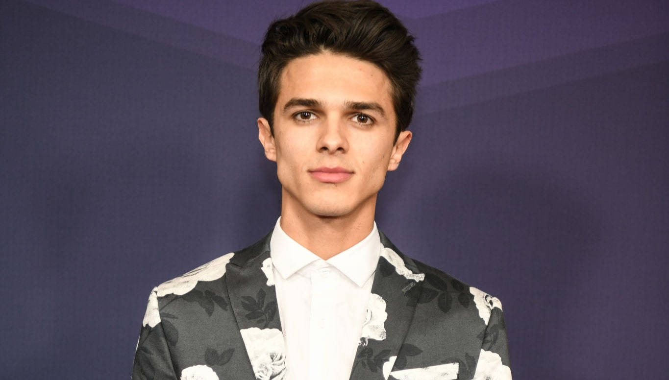 Brent Rivera 花紋西裝照 壁紙 — 一位身穿花卉圖案西裝的年輕男子，在純紫色背景和柔和的工作室燈光下自信地站立。