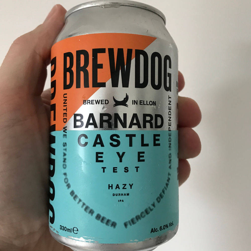 BrewDog Barnard Castle Eye Test 啤酒罐 壁紙 — 一隻手拿著一罐 BrewDog Barnard Castle Eye Test hazy IPA，帶有醒目的橙色和藍綠色品牌標識，背景為純白色。