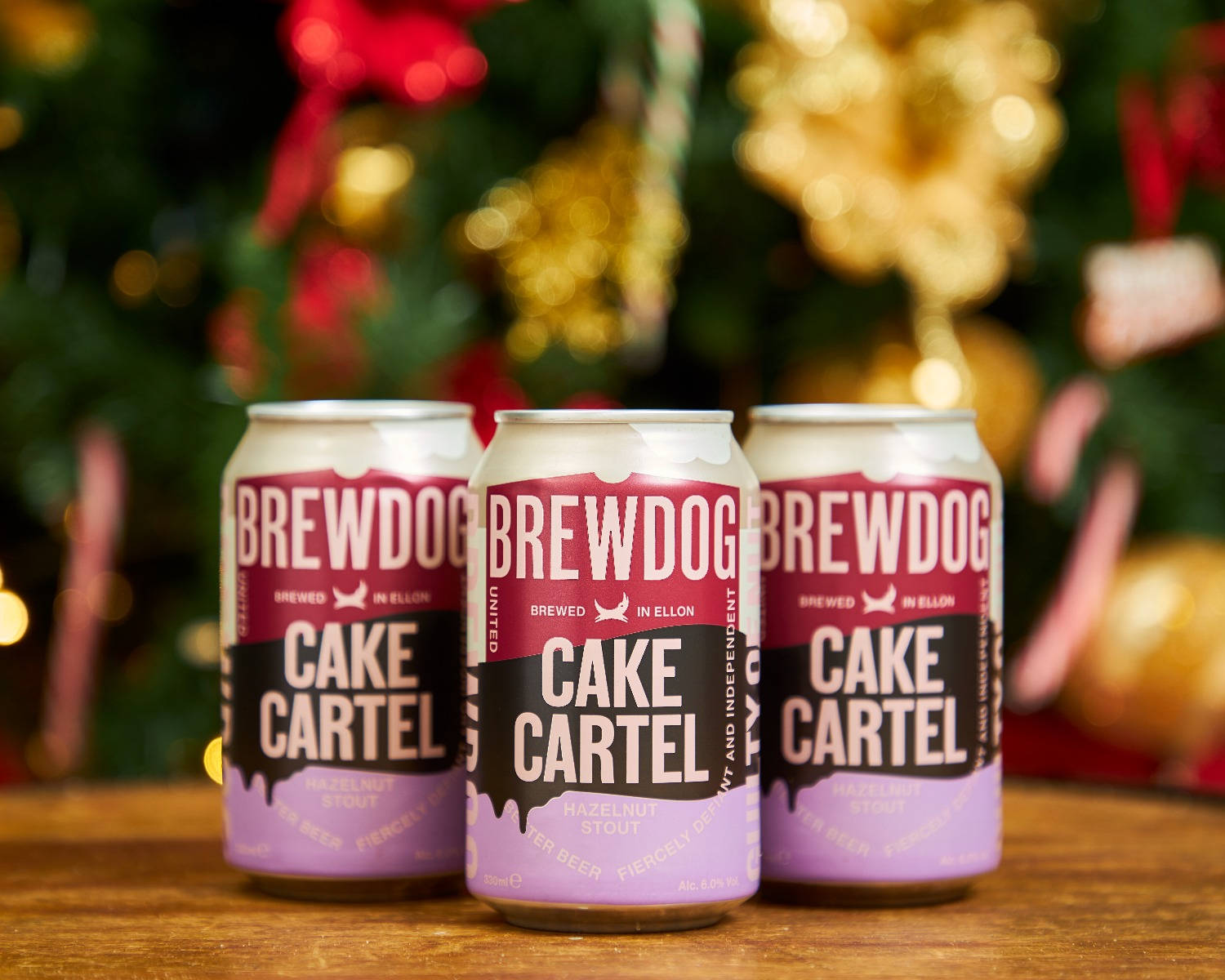 BrewDog Cake Cartel 啤酒罐 壁紙 — 三罐BrewDog Cake Cartel啤酒放在木質表面上，背景是節日氣氛的模糊聖誕樹。