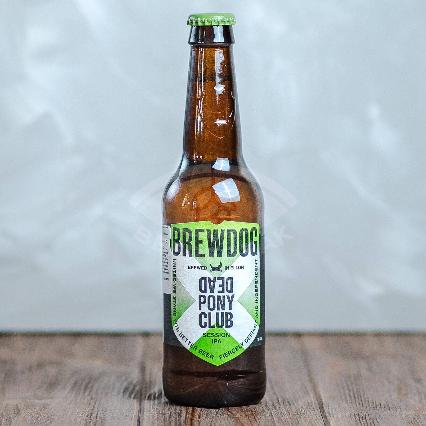 BrewDog Dead Pony Club 啤酒瓶 壁紙 — 一個棕色玻璃 BrewDog Dead Pony Club Session IPA 啤酒瓶，帶綠色瓶蓋，放在木質表面上，背景為柔和的灰色。