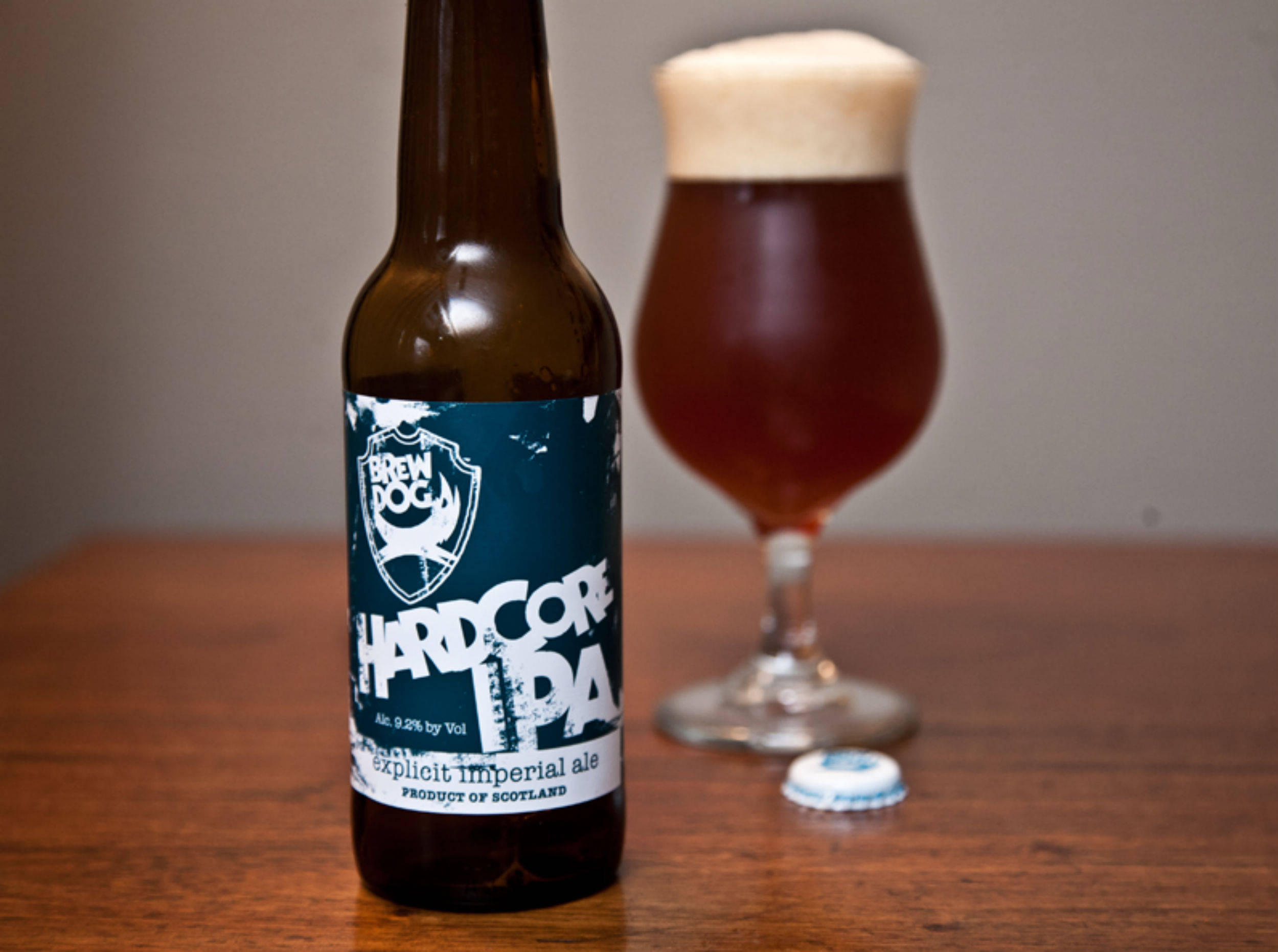 BrewDog Hardcore IPA 壁紙 — 一瓶BrewDog Hardcore IPA棕色啤酒放在木桌上，旁邊有一杯帶有泡沫的琥珀色啤酒。