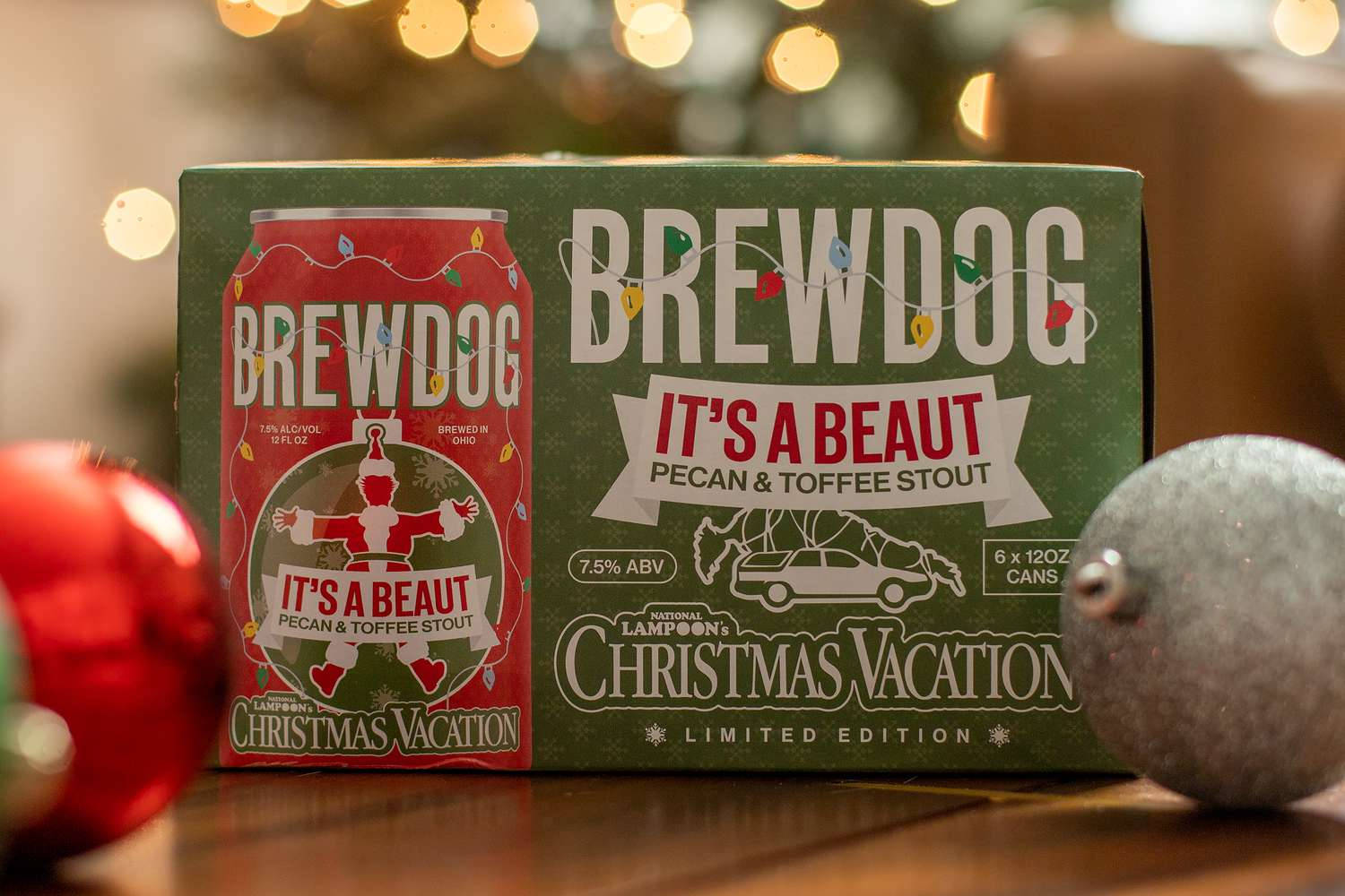 BrewDog It's A Beaut 限量包裝 壁紙 — 一個節日氣氛的BrewDog Christmas Vacation啤酒盒和罐子放在木桌上，旁邊有紅色和銀色的裝飾品，背景是溫暖的散景燈光。