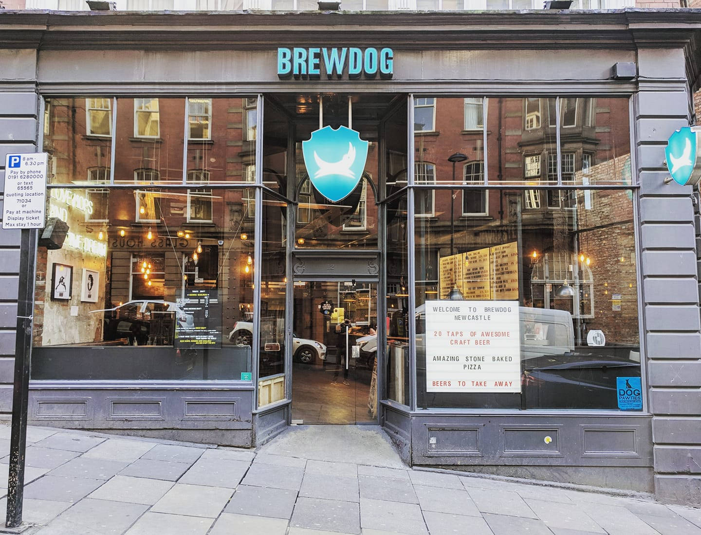 BrewDog 伯明翰分店外觀 壁紙 — BrewDog 啤酒廠店面，大型玻璃窗反射磚建築和街道標誌，在日光下。