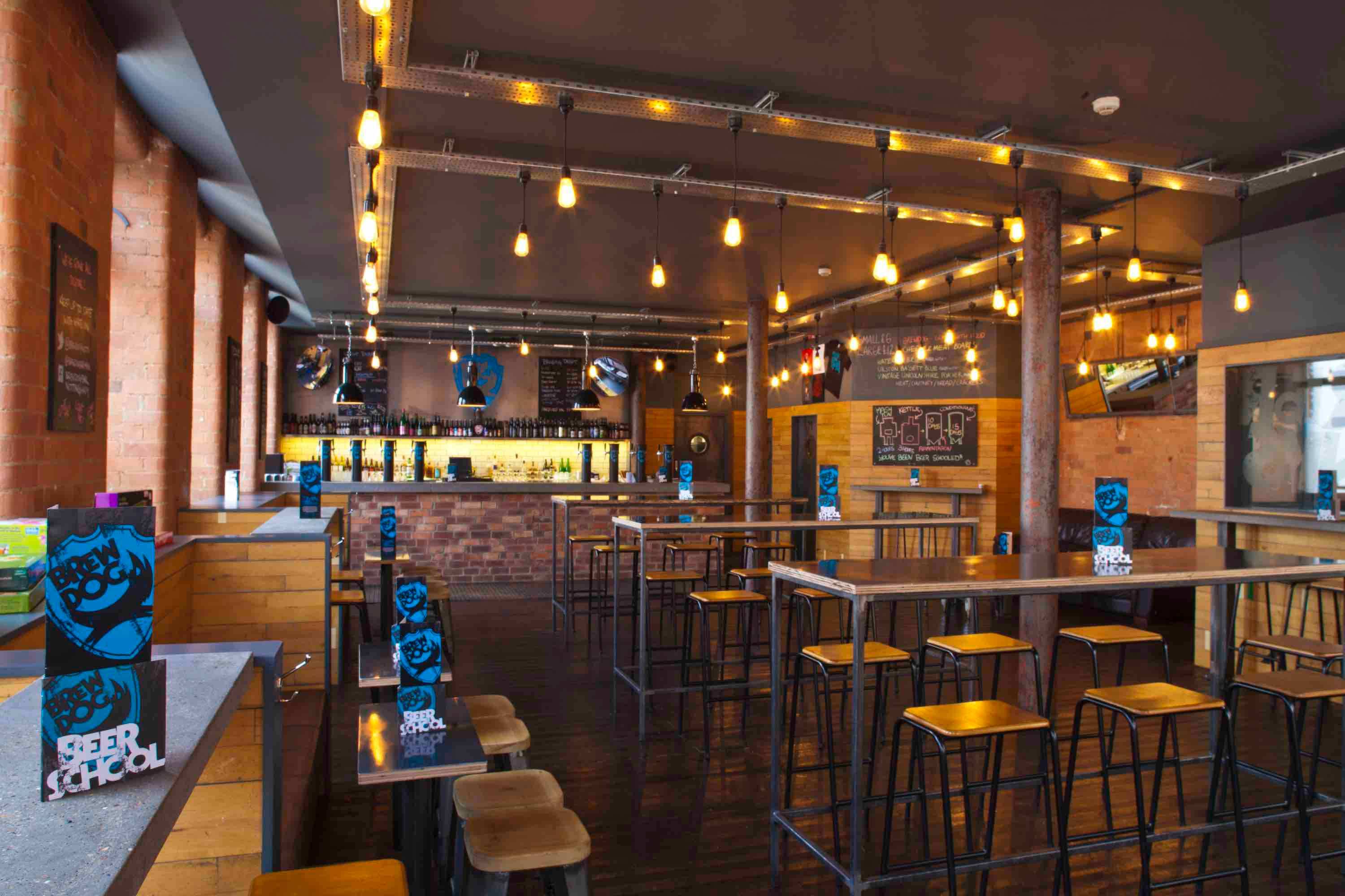 BrewDog 倫敦諾丁漢店內裝潢 壁紙 — 燈光溫暖的現代釀酒廠品酒室，設有裸露磚牆、木桌、吊燈和吧檯後方的啤酒龍頭。