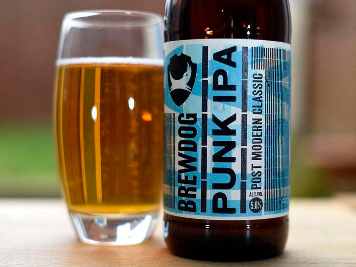 BrewDog 啤酒瓶與酒杯 壁紙 — 一瓶BrewDog Punk IPA放在木質表面上，旁邊是一個裝滿金黃色啤酒和白色泡沫的玻璃杯。