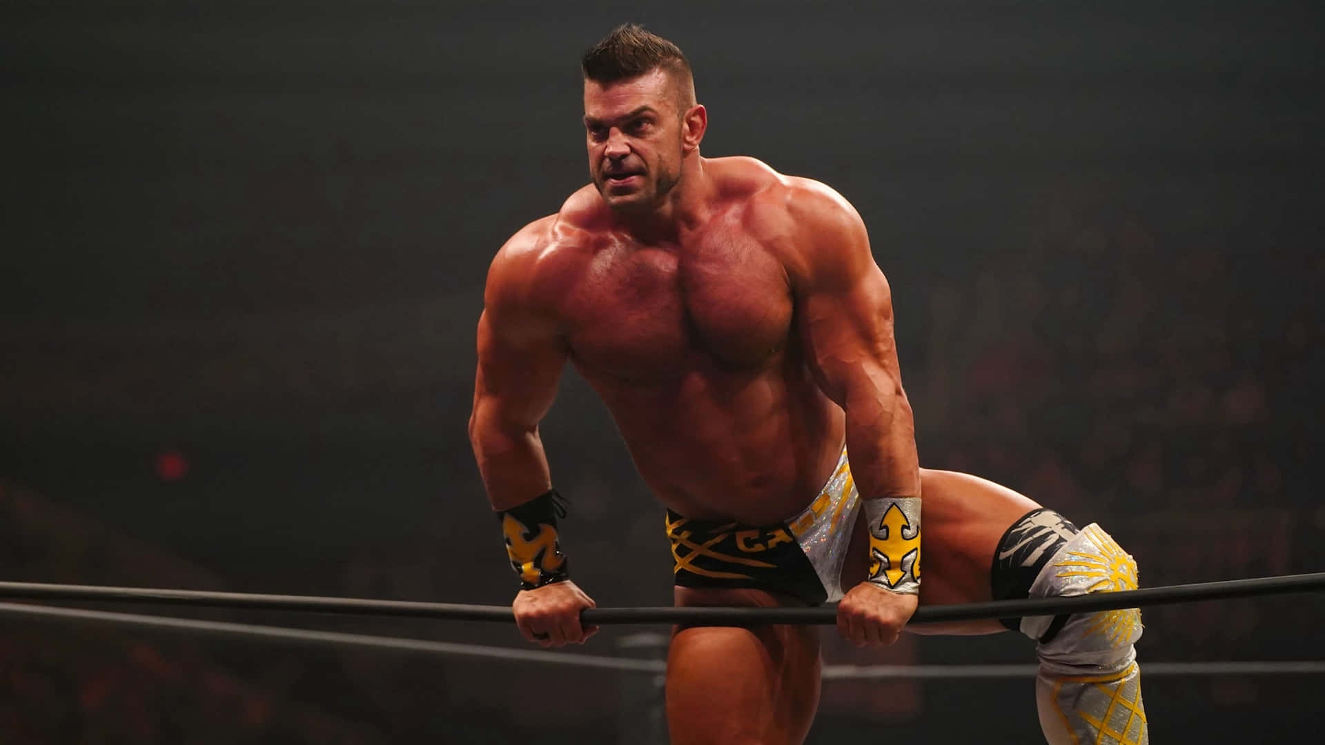 職業摔角手 Brian Cage 展現力量 壁紙 — 一位肌肉發達的摔角手在明亮的場館燈光下，專注地抓住擂台繩索。