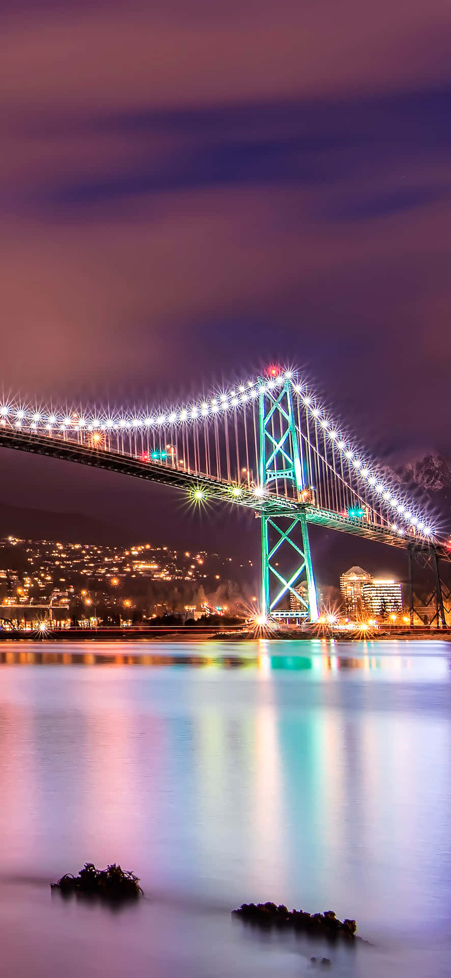 夜晚中明亮照明的吊橋，平靜水面上的倒影和紫色天空。