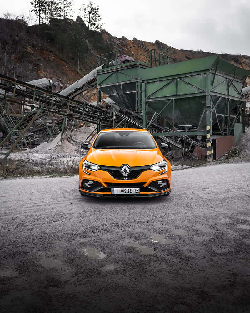 Renault Scenic 桌布 壁紙 — 一輛亮橙色的雷諾跑車大膽地停在濕漉漉的瀝青上，前方是陰天下一座破敗的工業採礦設施。